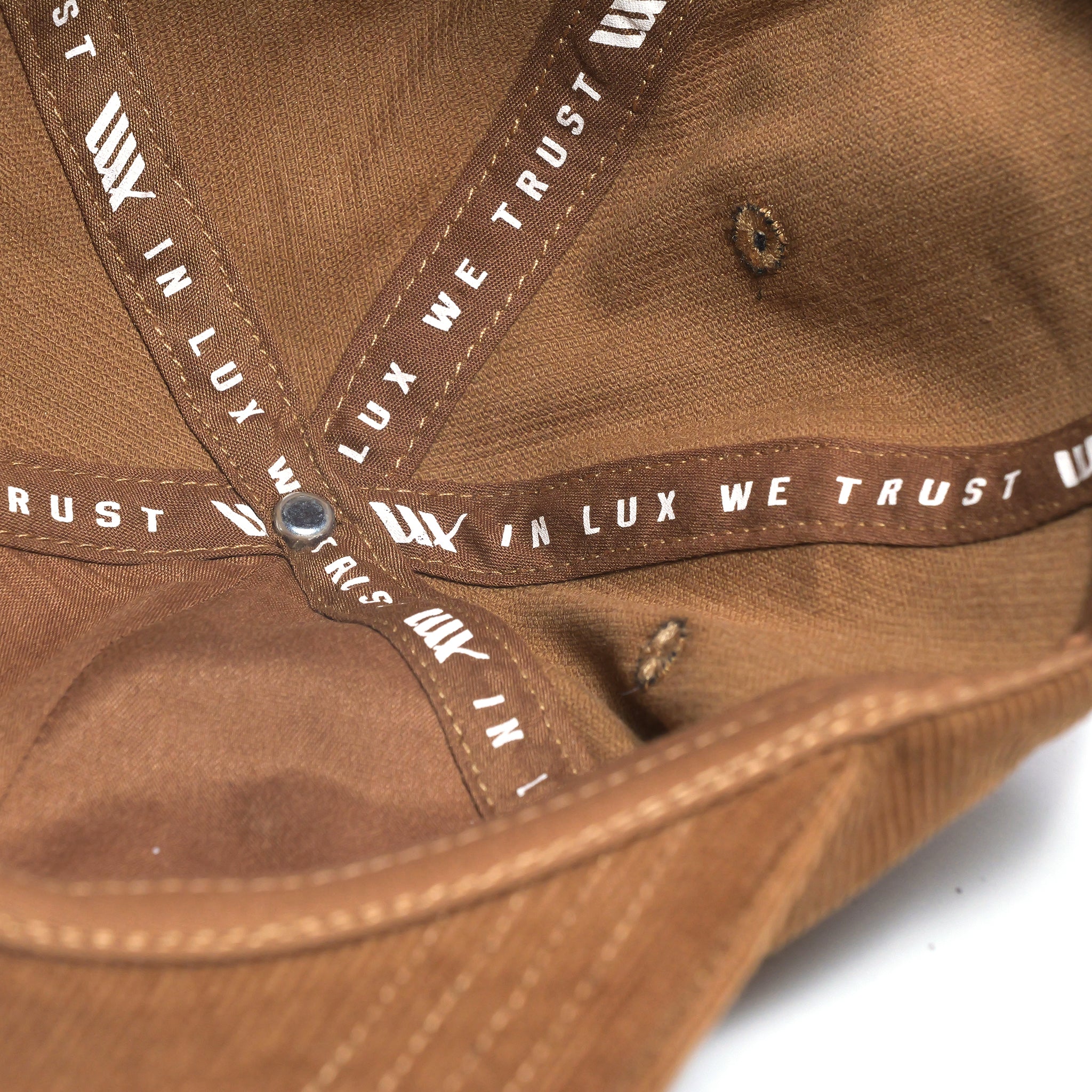 Close-up of the LUXBMX Outfield Cap Brown interior, highlighting the corduroy crown, detailed stitching, and a ribbon with repeated "IN LUX WE TRUST" text.