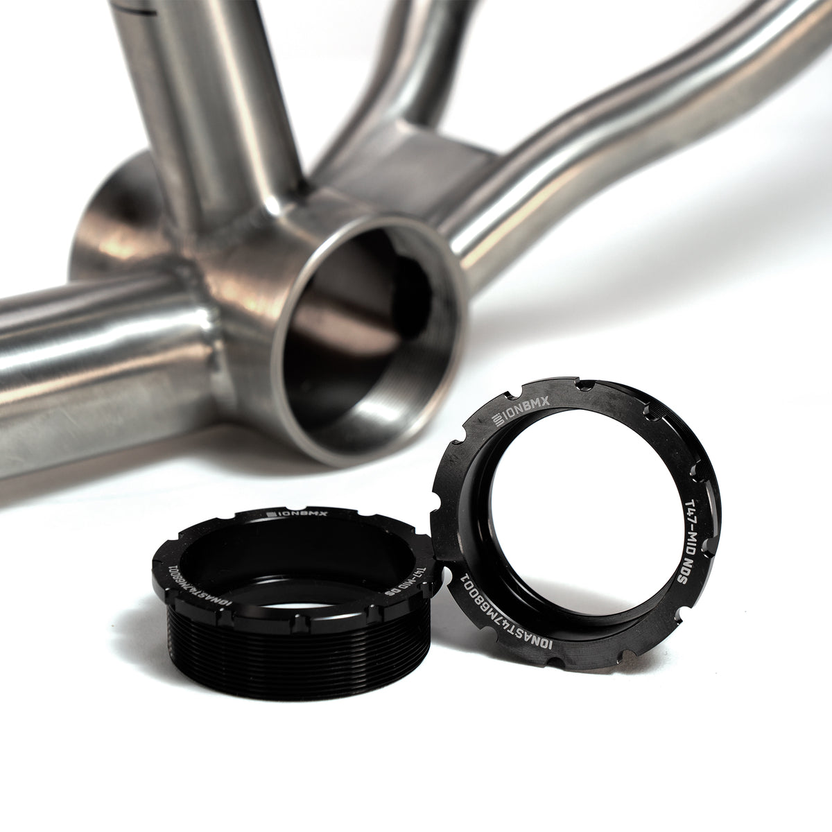A close-up of the ION BMX Ti22 Titanium 22 Inch Frame's bottom bracket shell with two black threaded cups nearby, designed for this model and featuring a precise headtube angle of 74 degrees.