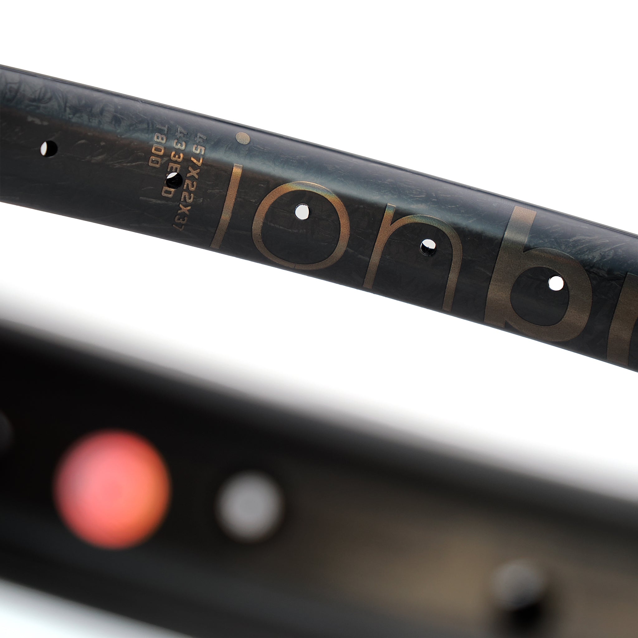 Close-up of the ION BMX C22 Carbon Fiber 22 Inch Braking Rim, highlighting part of the brand name, spoke holes, and a section with technical specifications printed on its lightweight surface.
