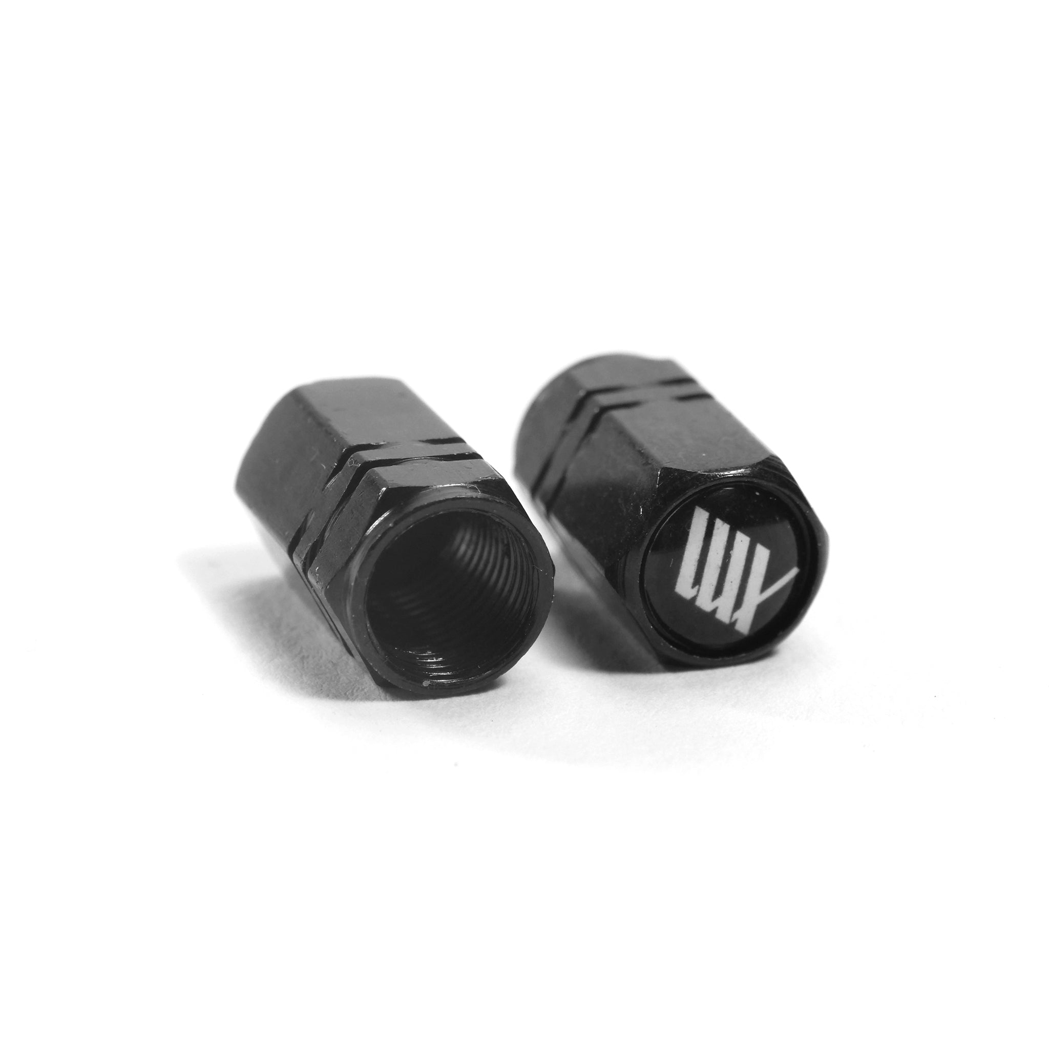 The LUXBMX Hex Logo Alloy Valve Cap (Pair) features two black hexagonal caps with a machined alloy build—one upright with a white "LUX" logo, the other showing the threaded interior. Ideal BMX accessories to upgrade your ride.
