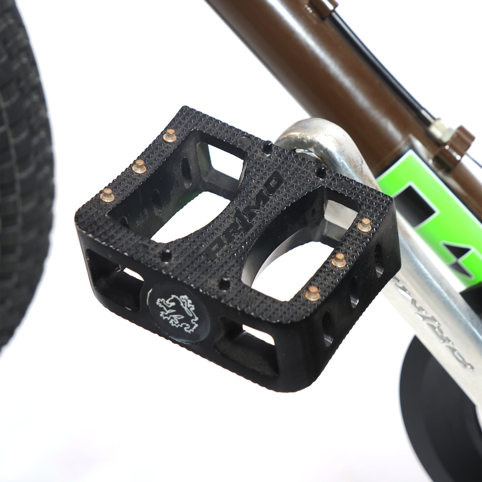 Close-up of a black DH Pro bicycle pedal on a silver crank arm, with part of the Terrible One Barcode Garrett Byrnes Custom 20 Inch Bike (2003) frame and tire visible in the background.
