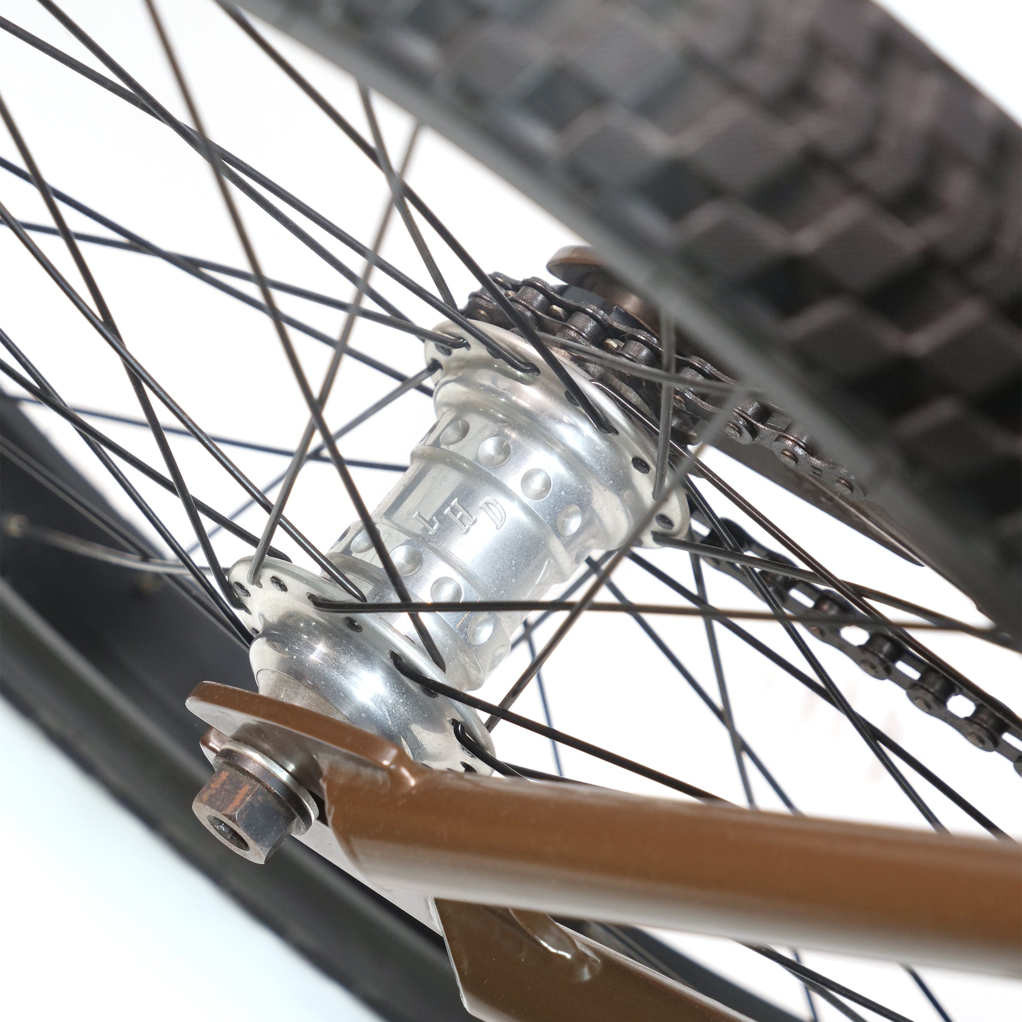 Close-up of a bicycle wheel showing the rear hub, spokes, tire, and part of the Terrible One Barcode Garrett Byrnes Custom 20 Inch Bike (2003) frame.