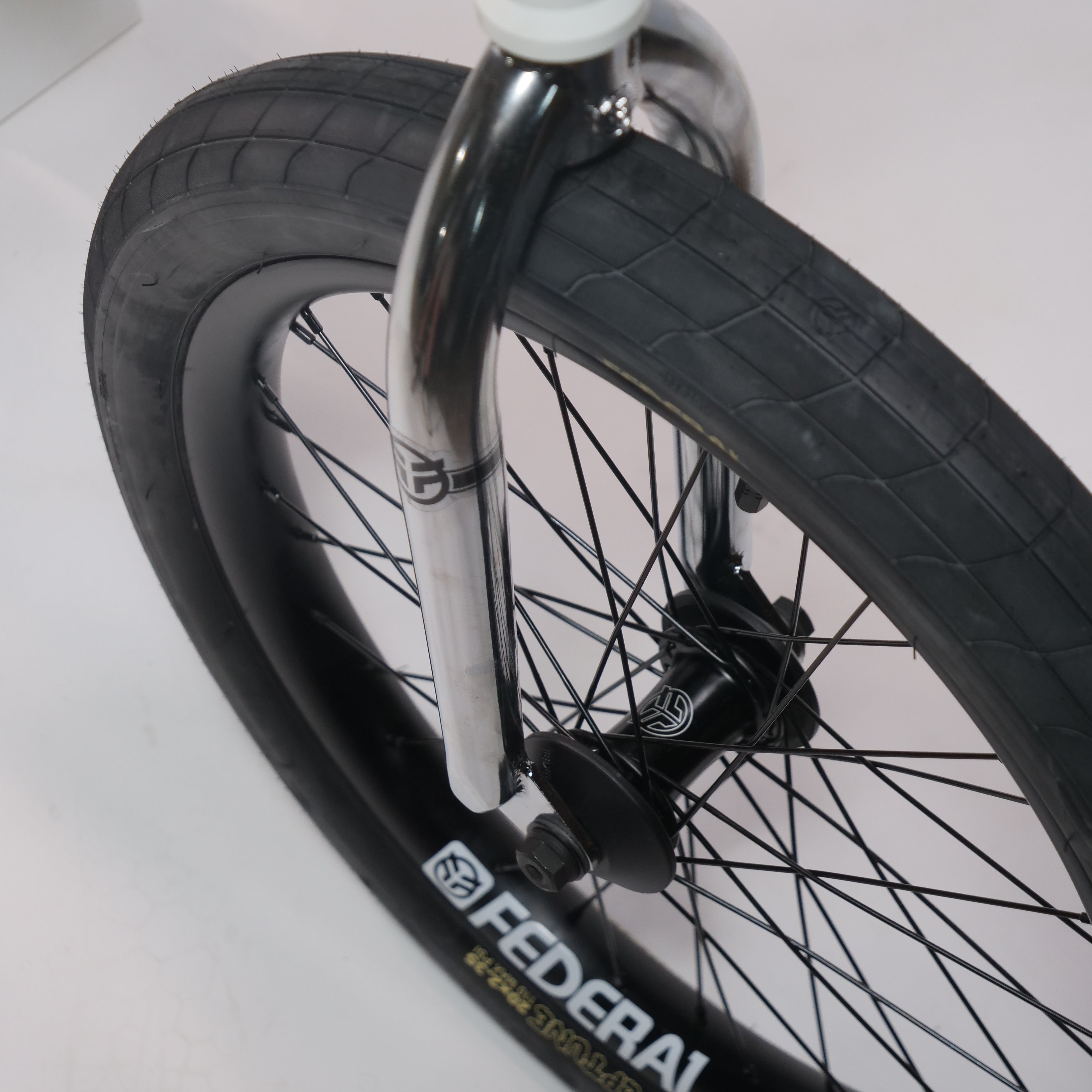 Close-up of the Federal Lacey x Chrome Custom 20 Inch Bike's front wheel, featuring a thick black tire, black spokes, silver Assault Forks, and "FEDERAL" branding on the rim.