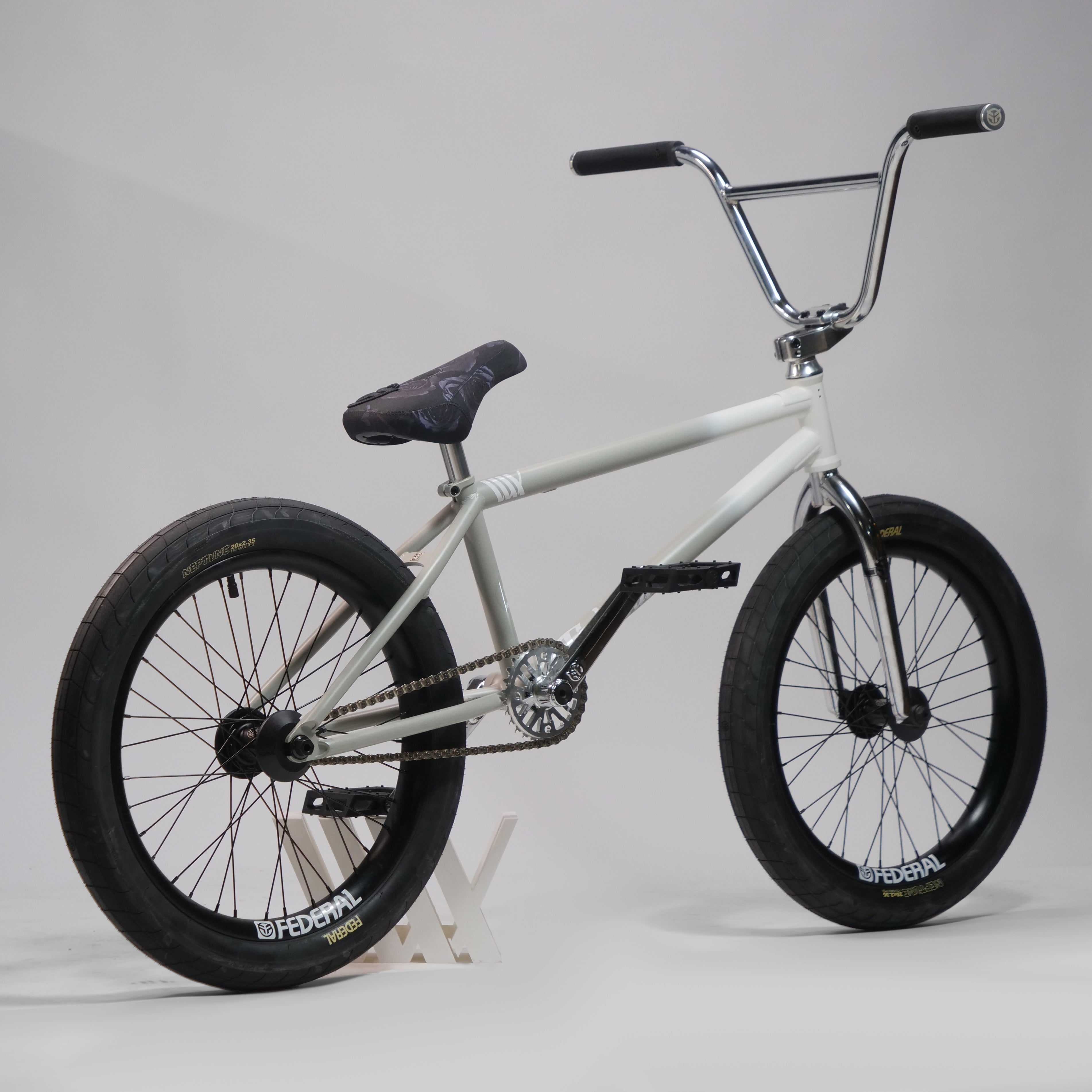The Federal Lacey x Chrome Custom 20 Inch Bike, featuring a white frame, black seat, and black tires, is displayed on a gray background with a simple stand supporting the rear wheel.