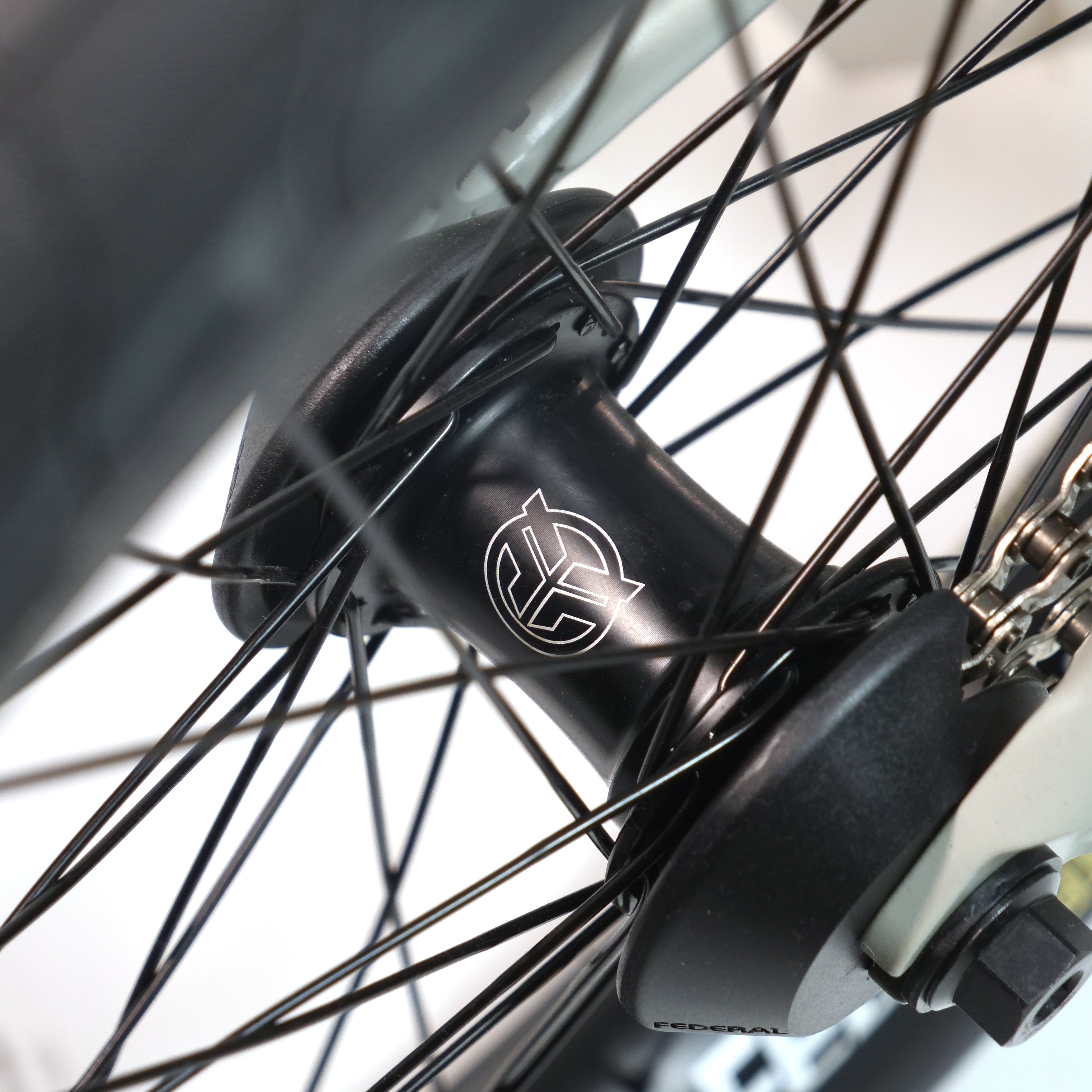 Close-up of the Federal Lacey x Chrome Custom 20 Inch Bike’s black wheel hub with silver logo, surrounded by black spokes and visible gear mechanism, showcasing signature BMX components.