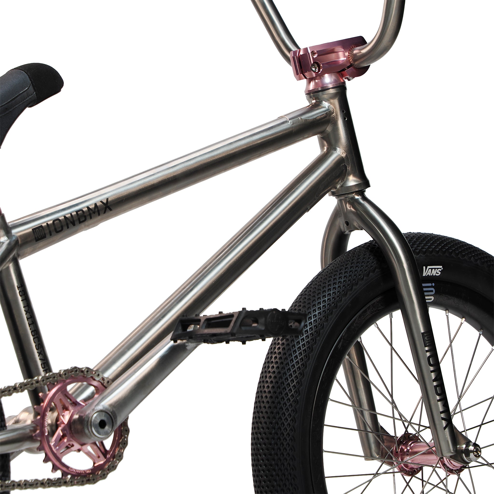 Close-up of the ION BMX Ti18 Custom Titanium 18 Inch Bike, featuring a metallic frame, pink crankset and headset, black pedal, and a black front tire with "Vans" branding—perfect for lightweight freestyle BMX riding.