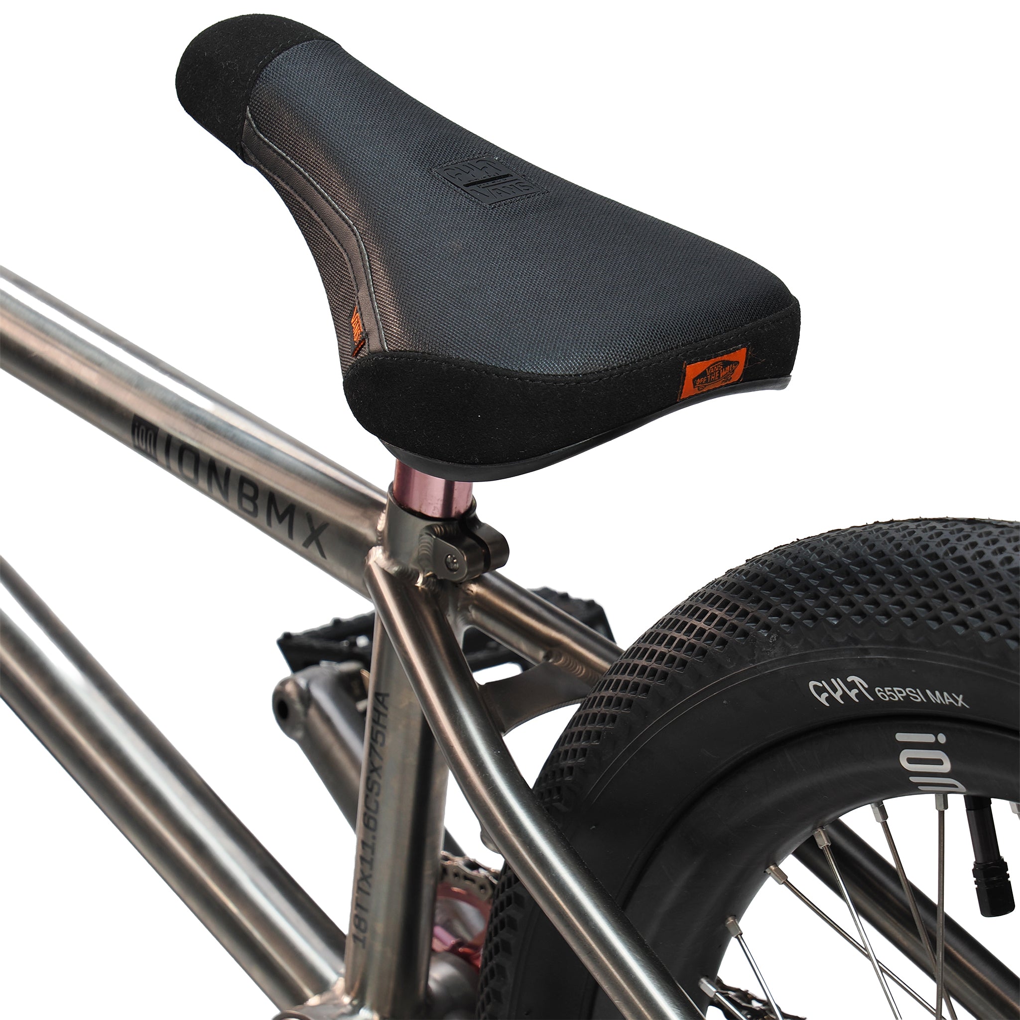 Close-up of a black BMX seat on the ION BMX Ti18 Custom Titanium 18 Inch Bike, highlighting its lightweight freestyle build. A knobby rear tire appears in the background, emphasizing the bike’s style and performance.
