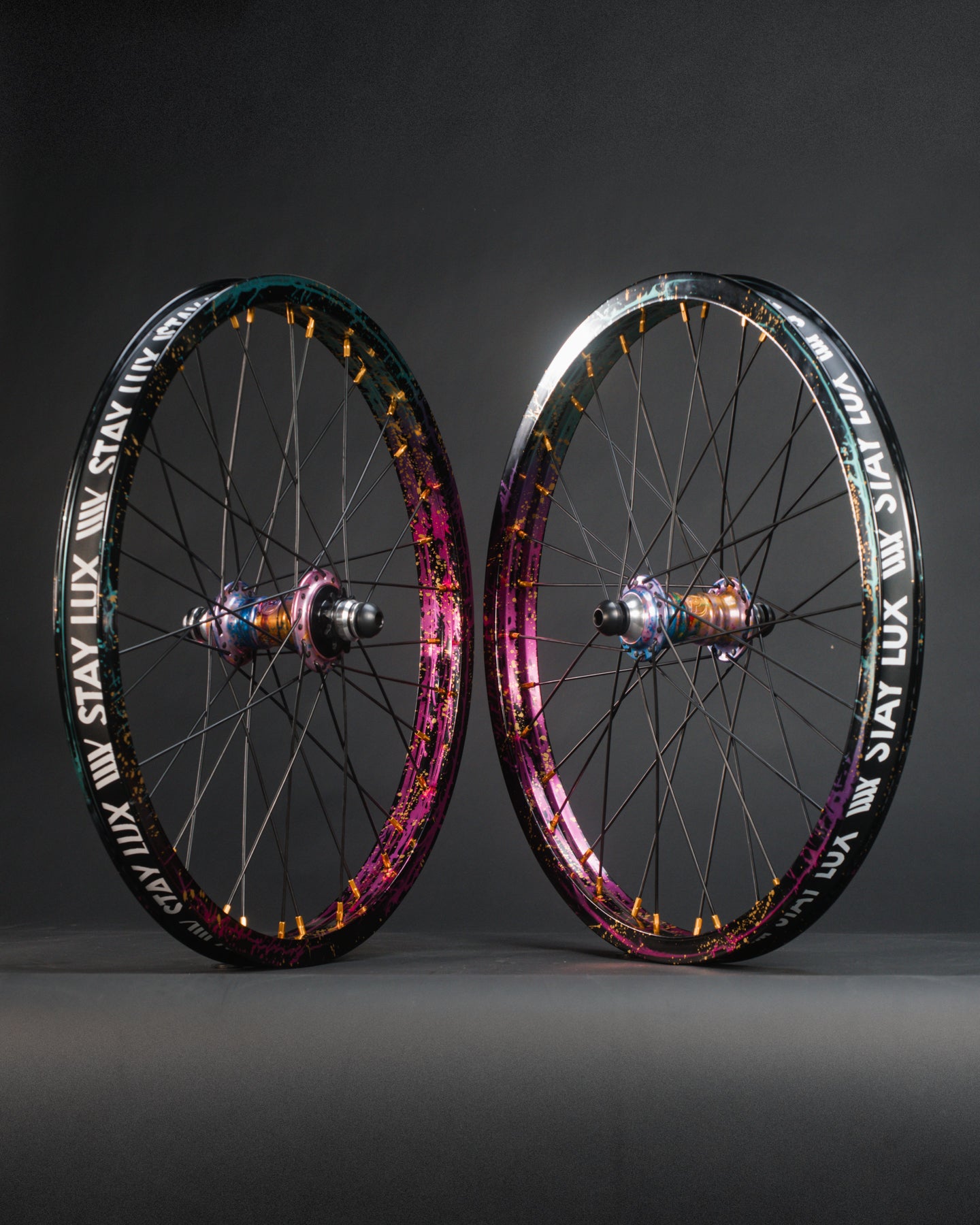 Two colorful bicycle wheels with black rims and metallic spokes, featuring BMX hubs, stand upright. The rims show “STAY LUX” in bold white text, highlighting the limited edition Profile x Odyssey Near Earth Objects Wheel Set.