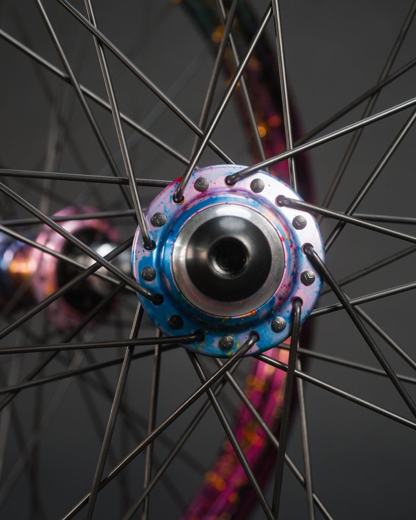 Close-up of the limited edition Profile x Odyssey Near Earth Objects Wheel Set, featuring silver spokes in a radial pattern and vibrant accents, set against a dark background.