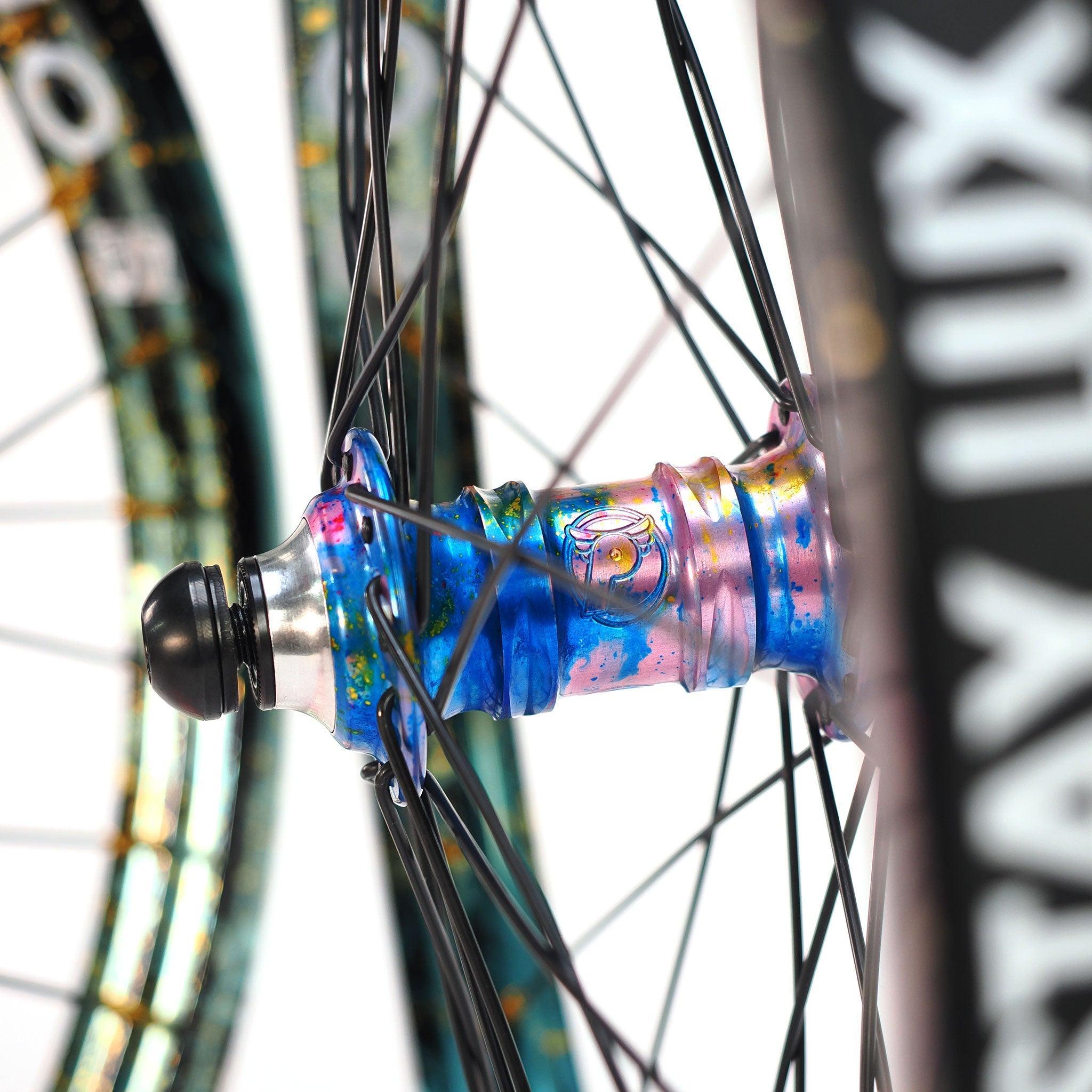 Close-up of the limited edition Profile x Odyssey Near Earth Objects Wheel Set featuring a colorful, iridescent BMX hub with black spokes and a partially visible rim, shown against a white background.