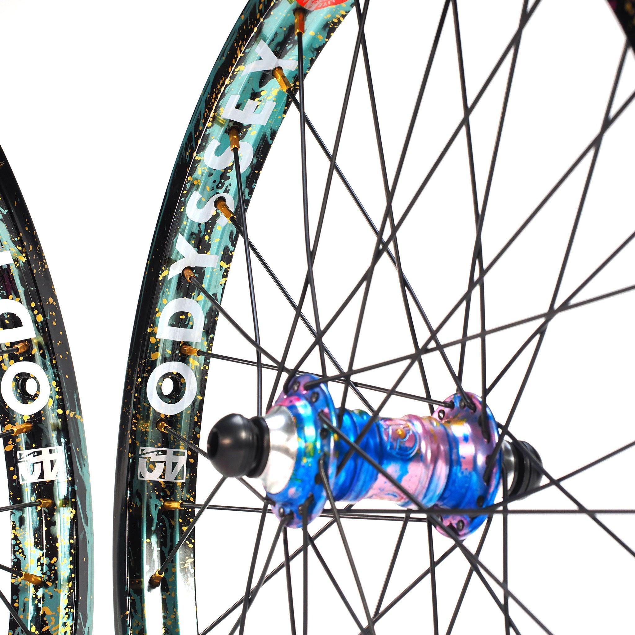 Close-up of two spoked bicycle wheels from the limited edition Profile x Odyssey Near Earth Objects Wheel Set; one has a vibrant BMX hub, the other displays the "Odyssey Hazard 40th Anniversary Rim.
