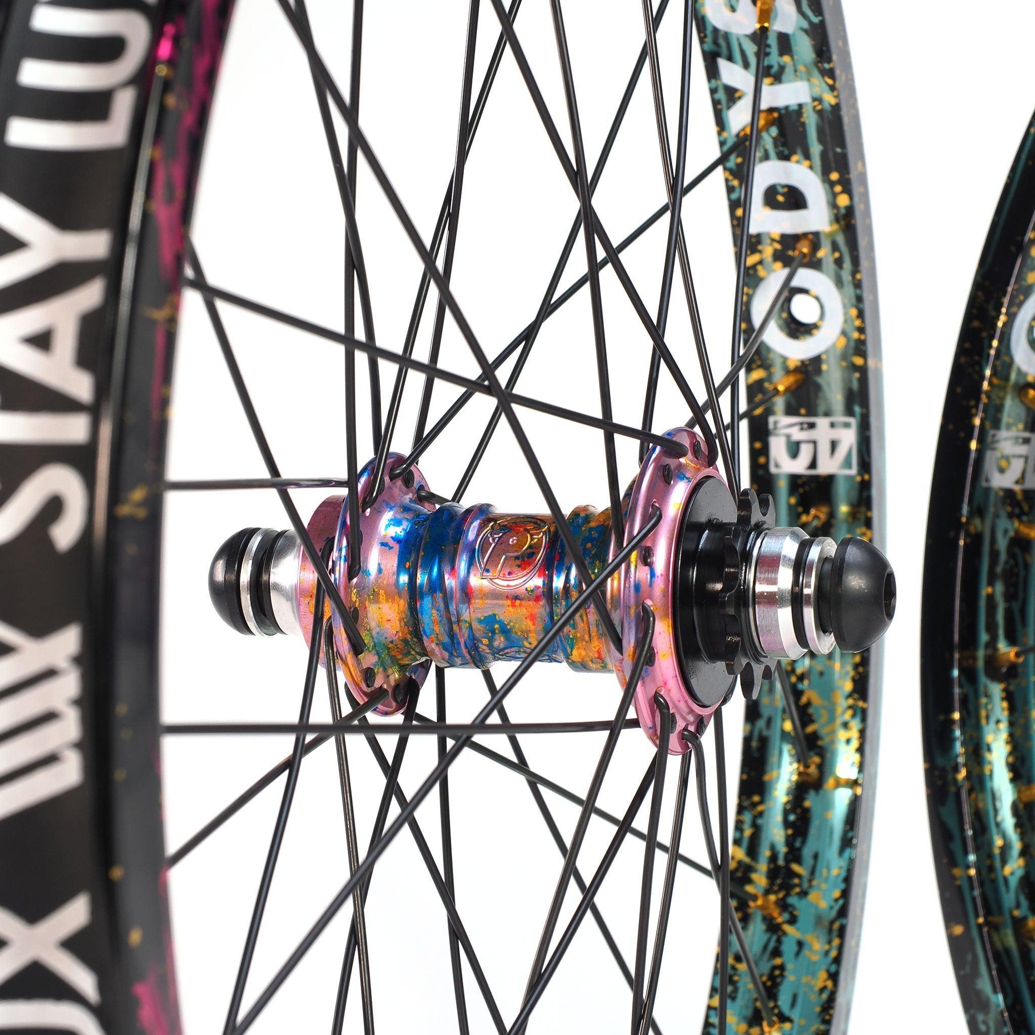 Close-up of two colorful BMX wheels from the limited edition Profile x Odyssey Near Earth Objects Wheel Set, featuring black spokes, patterned rims, and a multicolored anodized hub.