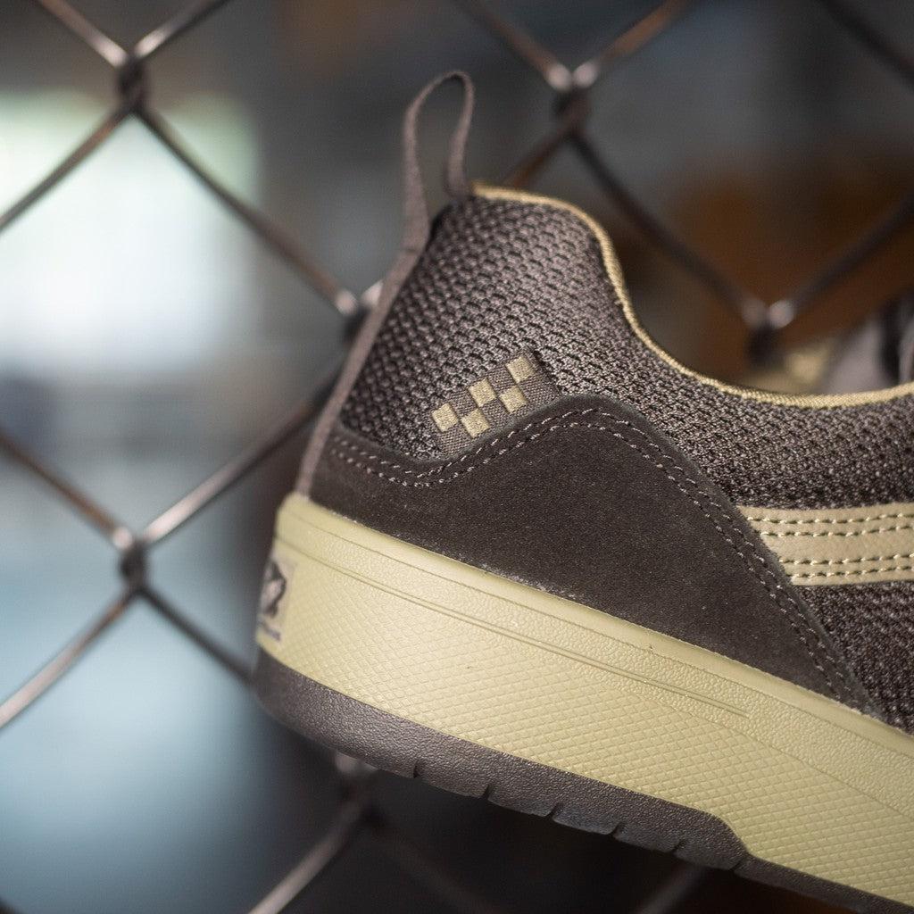 A pair of Vans Zahba Shoes Fatigue/Black, showcasing their sustainability and boardfeel, dangle effortlessly from a chain link fence.