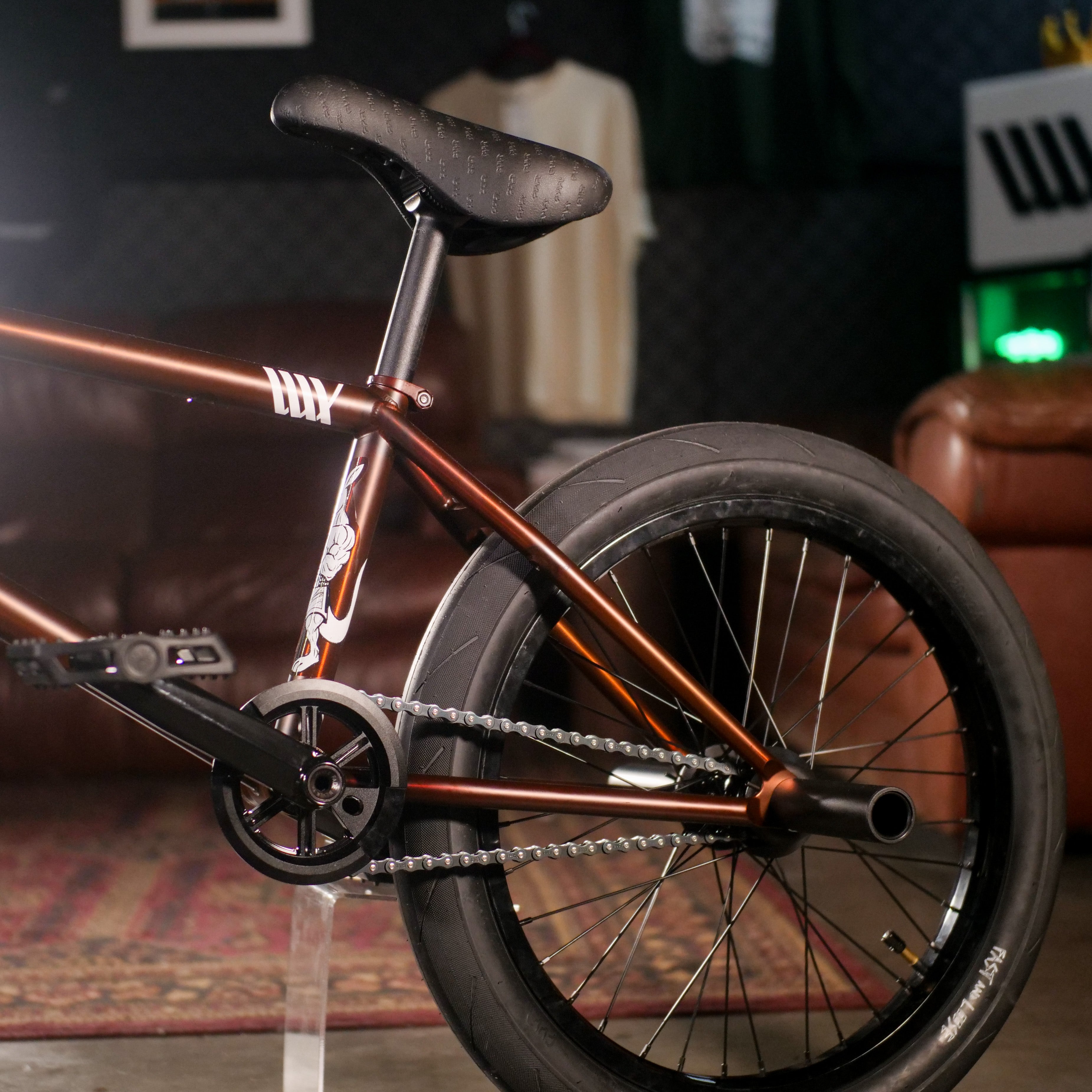 Close-up of the rear wheel, seat, and chain of a BMX bike with the Cult Dak X Eclat Custom 'Pat Freyne Signature' frame in copper, displayed indoors on a patterned rug—highlighting essential BMX components.
