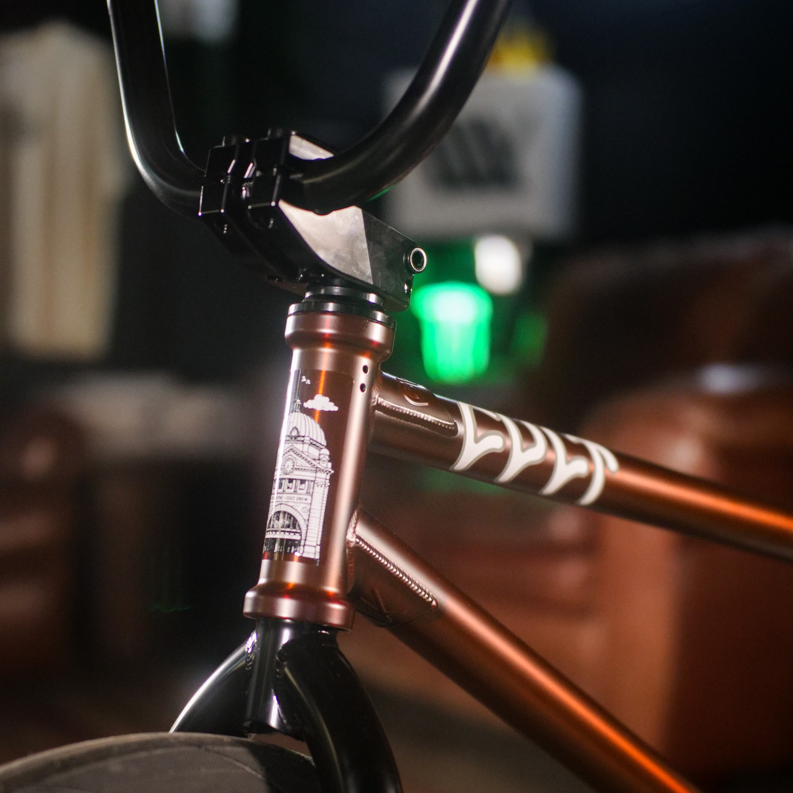 Close-up of a BMX bike’s front frame and handlebars, showing an architectural illustration sticker, metallic brown finish, and signature parts from the Cult Dak X Eclat Custom 'Pat Freyne Signature'.