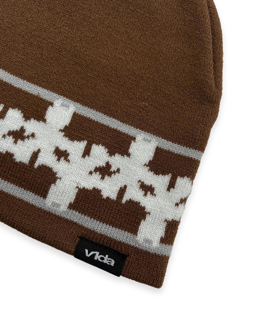Close-up of the V1da Pattern Beanie, a brown low-fit winter hat featuring a white and gray geometric design and a black "vida" tag on the edge.