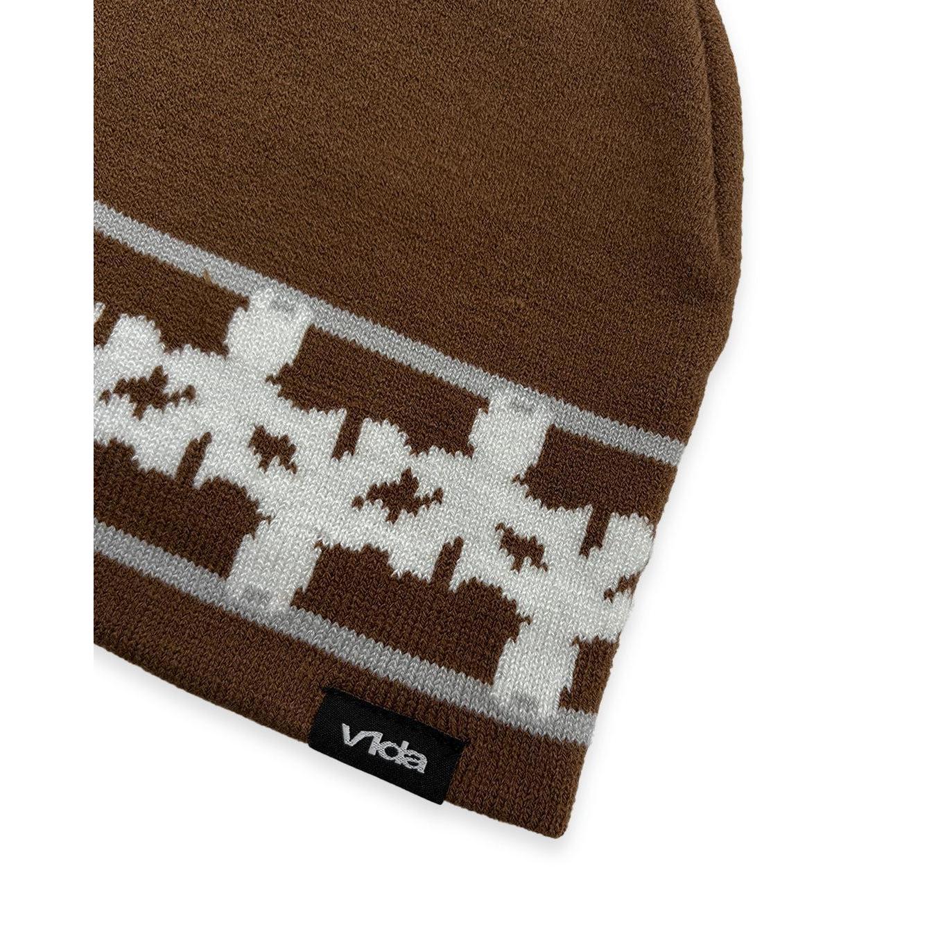 Close-up of the V1da Pattern Beanie, a brown low-fit winter hat featuring a white and gray geometric design and a black "vida" tag on the edge.
