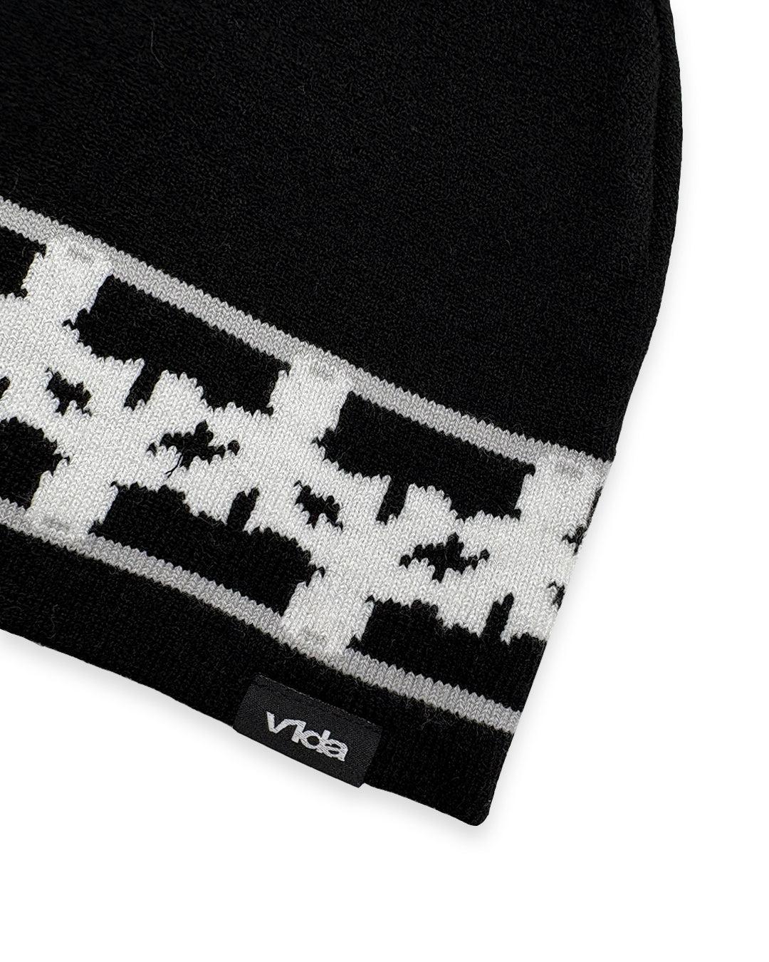 The V1da Pattern Beanie is a black skully hat with a white geometric design and a subtle black tag featuring "Vida" near the edge—ideal for stylish winter wear.