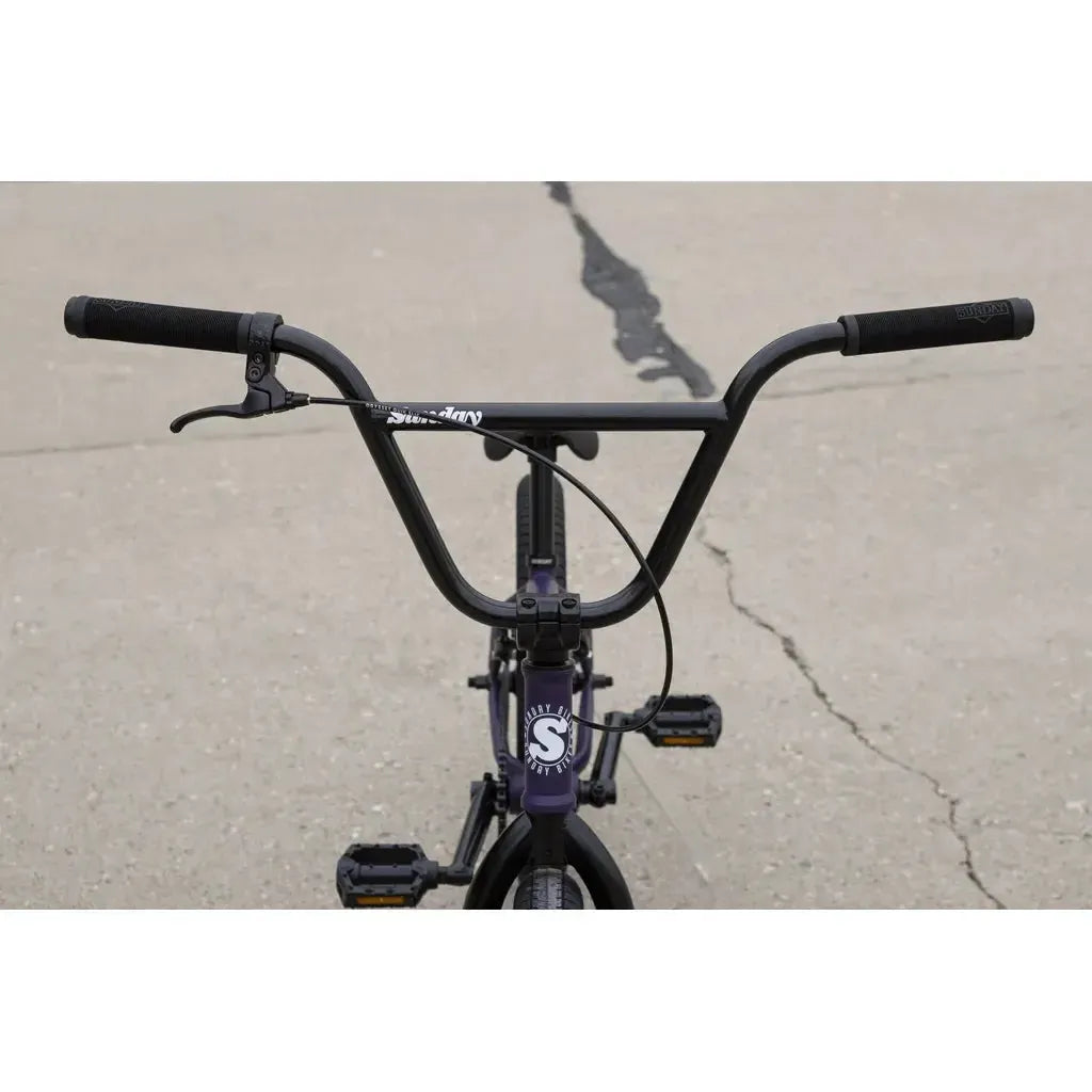 Close-up of a black Sunday Primer 20 Inch Bike kids BMX handlebar and front wheel on cracked concrete, perfect for anyone seeking their first beginner's BMX bike.