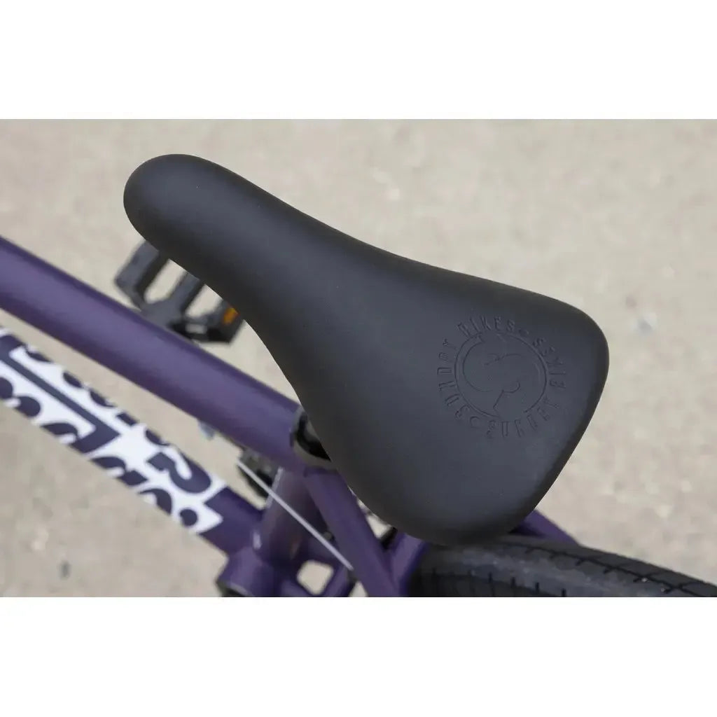 Close-up of a black bike seat with "Sunday Bikes" branding, mounted on a purple Sunday Primer 20 Inch Bike frame with patterned decals—perfect for kids or beginner BMX setups.
