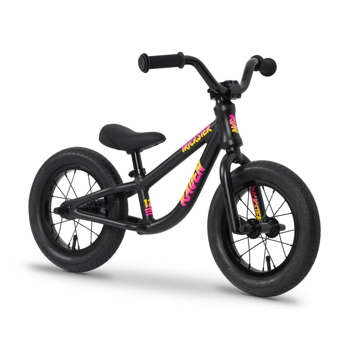 The Raven Trickster Alloy 12 Inch Balance Bike is a black kids' bike with thick tires, sealed bearings for smooth rides, no pedals, and features colorful "Krusher" graphics on the frame and fork.