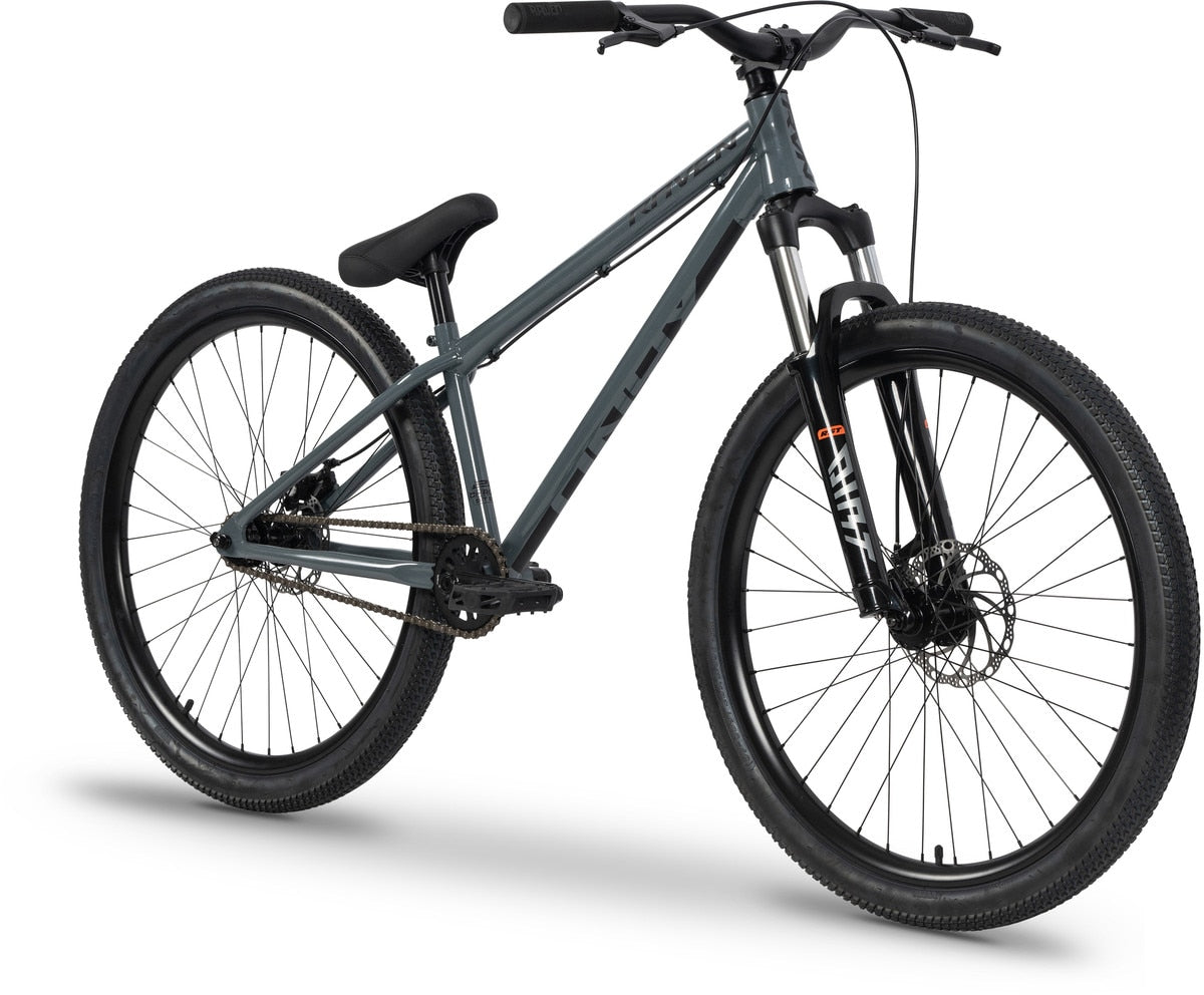 The Raven Onyx 26 Inch Dirt Jumper Bike, featuring a gray Chromoly frame, thick black tires, front suspension fork, flat handlebars, single gear, and disc brakes, is displayed on a white background.
