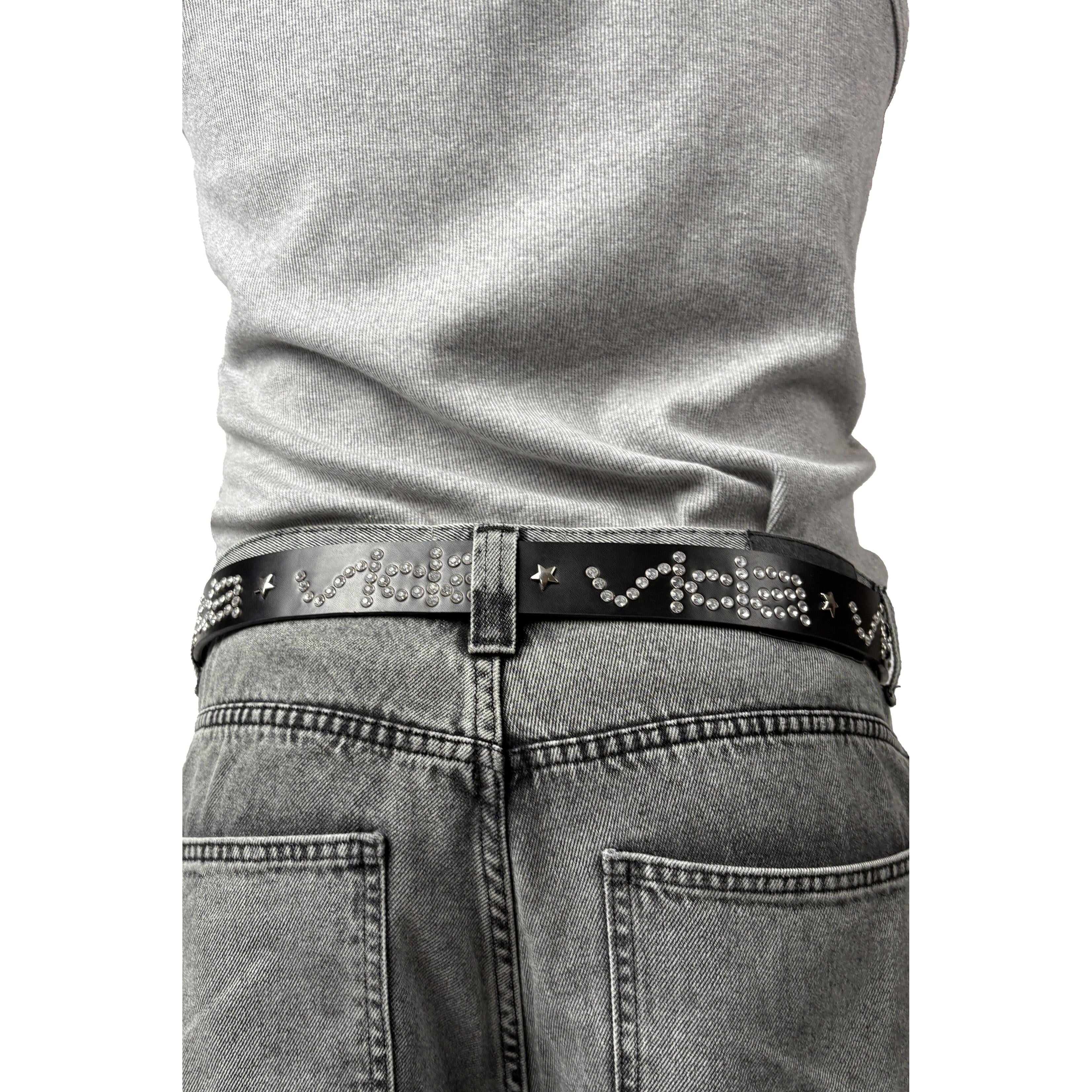 Person wearing a gray shirt tucked into faded gray jeans, styled with the V1da Studded Leather Belt featuring metallic text, star-shaped studs, and silver rivets for added edge.