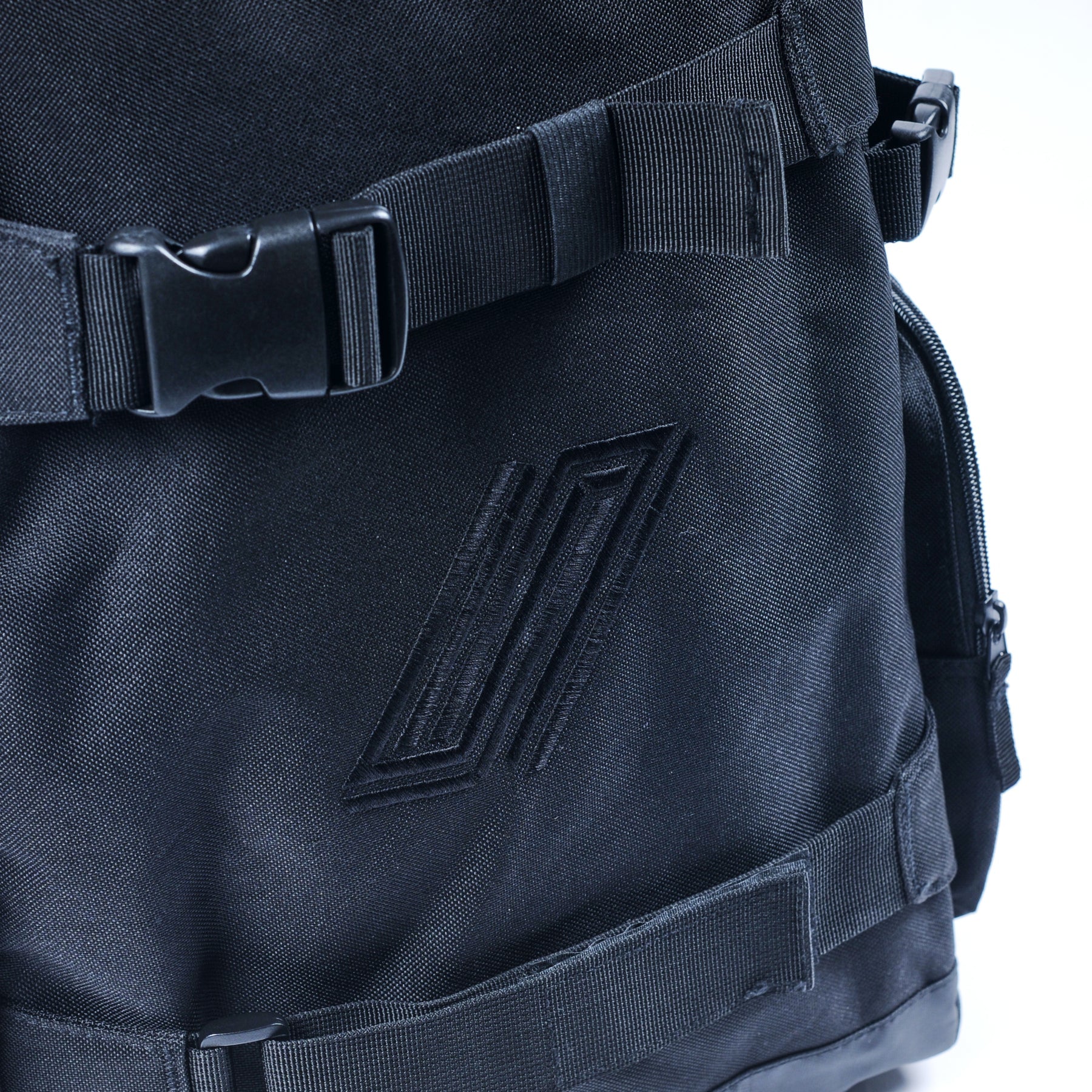 Close-up of a black United Dayward Backpack featuring buckle straps, skateboard carry straps, and a stitched geometric logo on the front.