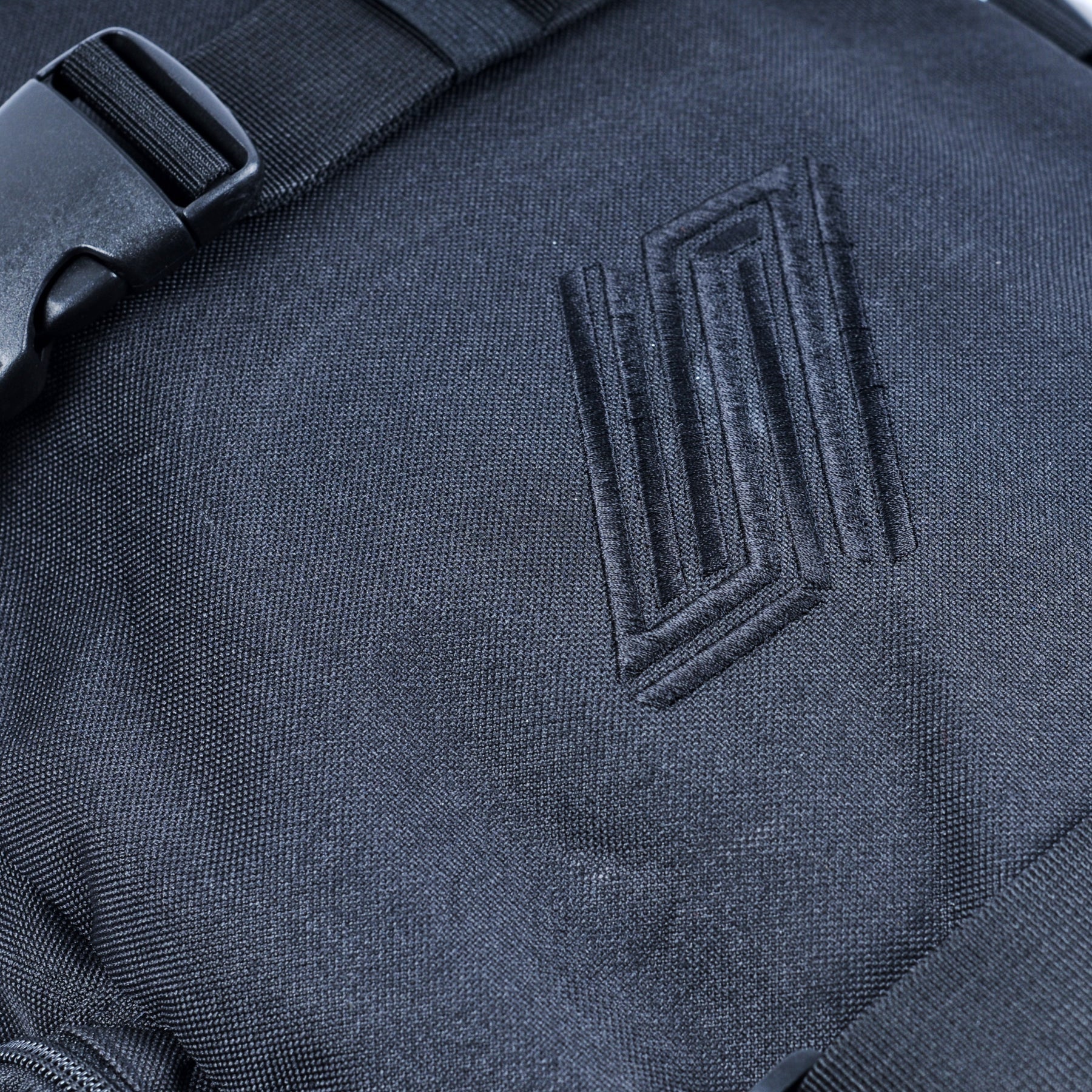 Close-up of the United Dayward Backpack in black, featuring a geometric embroidered logo, plastic buckle strap, and convenient skateboard carry straps.