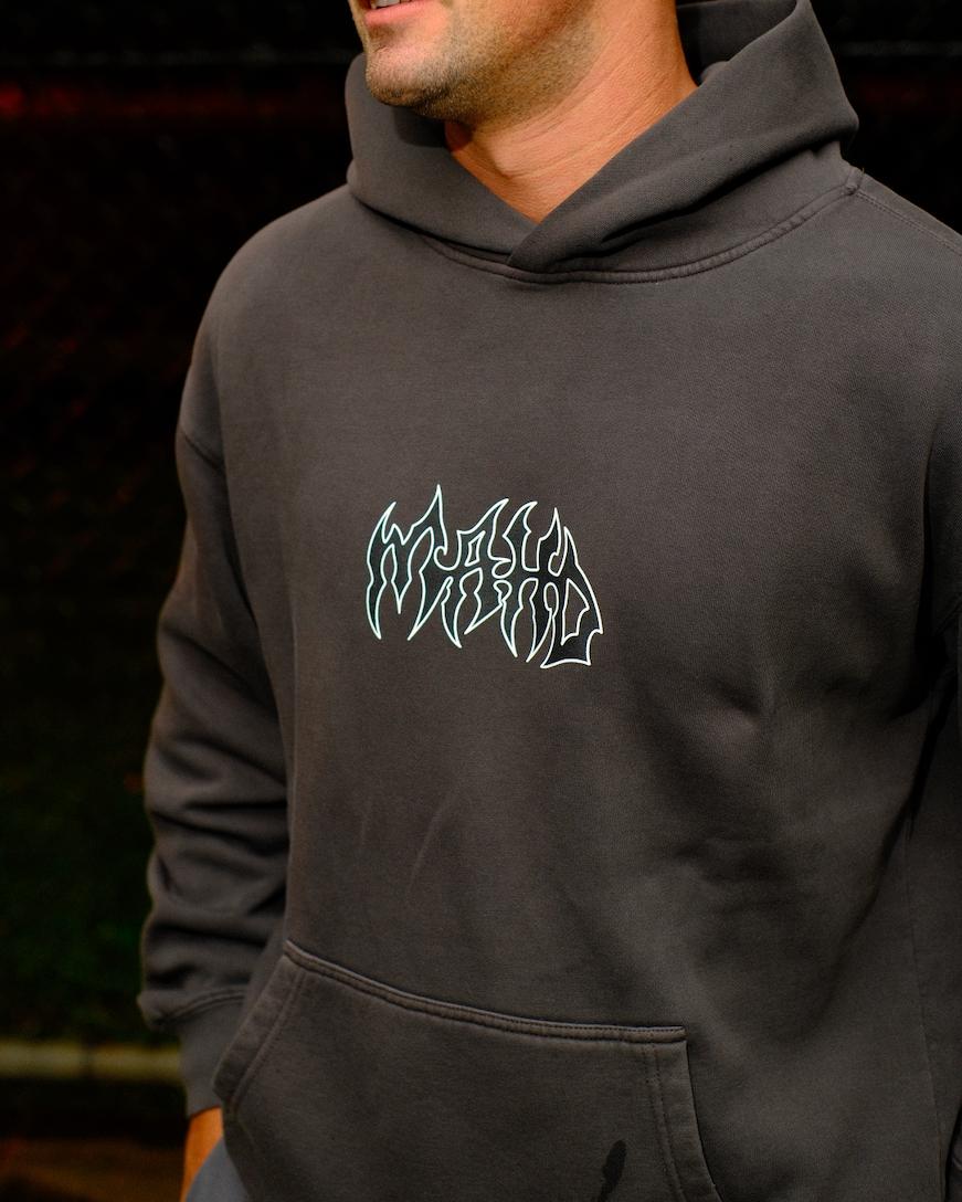 A person wearing the Mahd Metal Hoodie, a dark gray hoodie featuring a stylized white graphic design on the chest, standing outdoors.