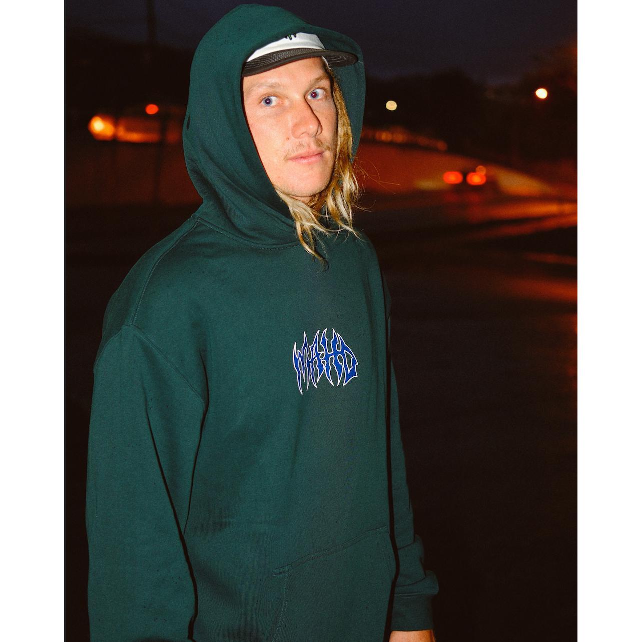 A person with long blond hair wears the Mahd Metal Hoodie and a cap, standing outside at night with blurred street lights in the background.