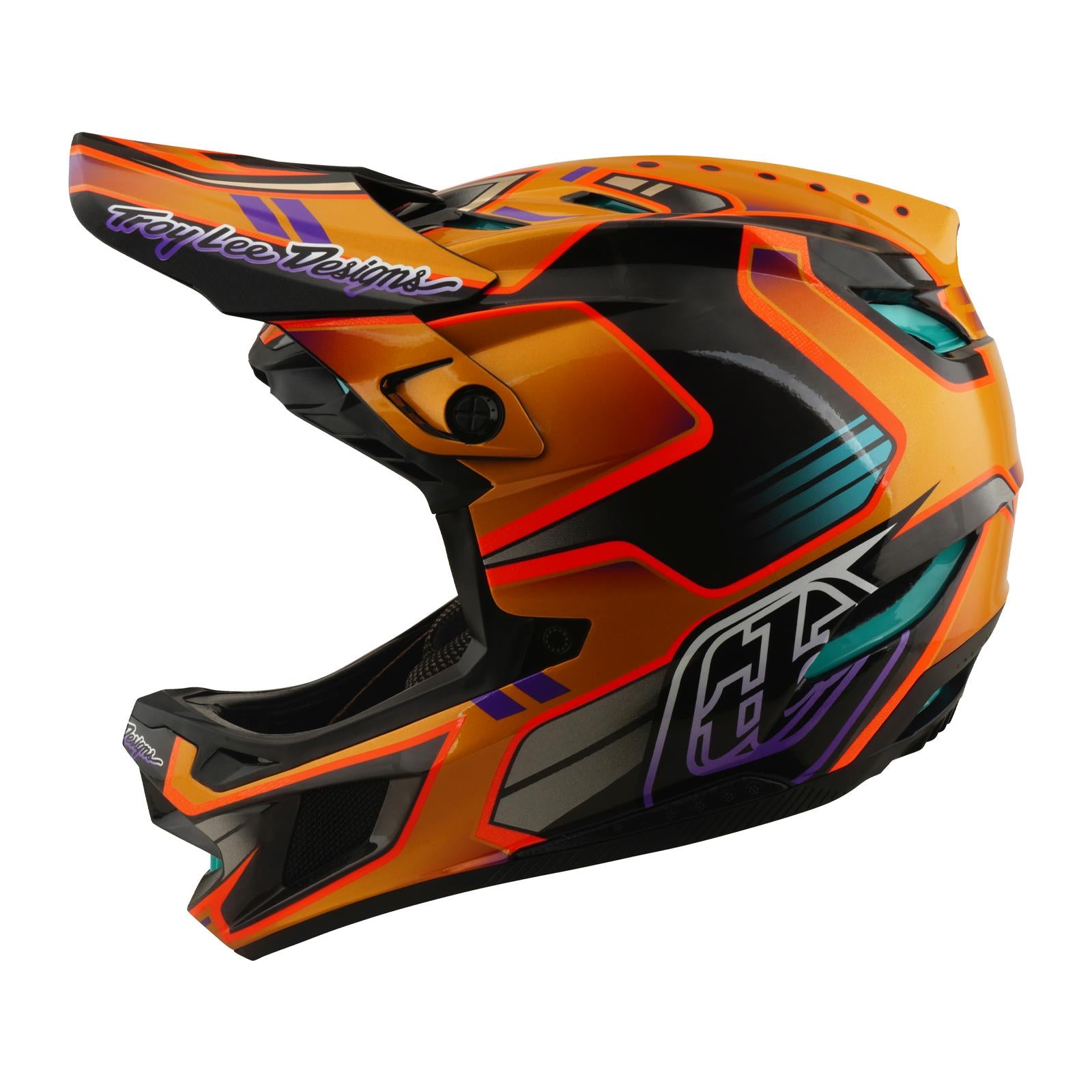 The TLD 26.1 D4 AS Carbon Helmet / Crest Gold is a full-face mountain biking helmet featuring geometric patterns, "Troy Lee Designs" on the visor, and advanced Mips protection for enhanced safety.
