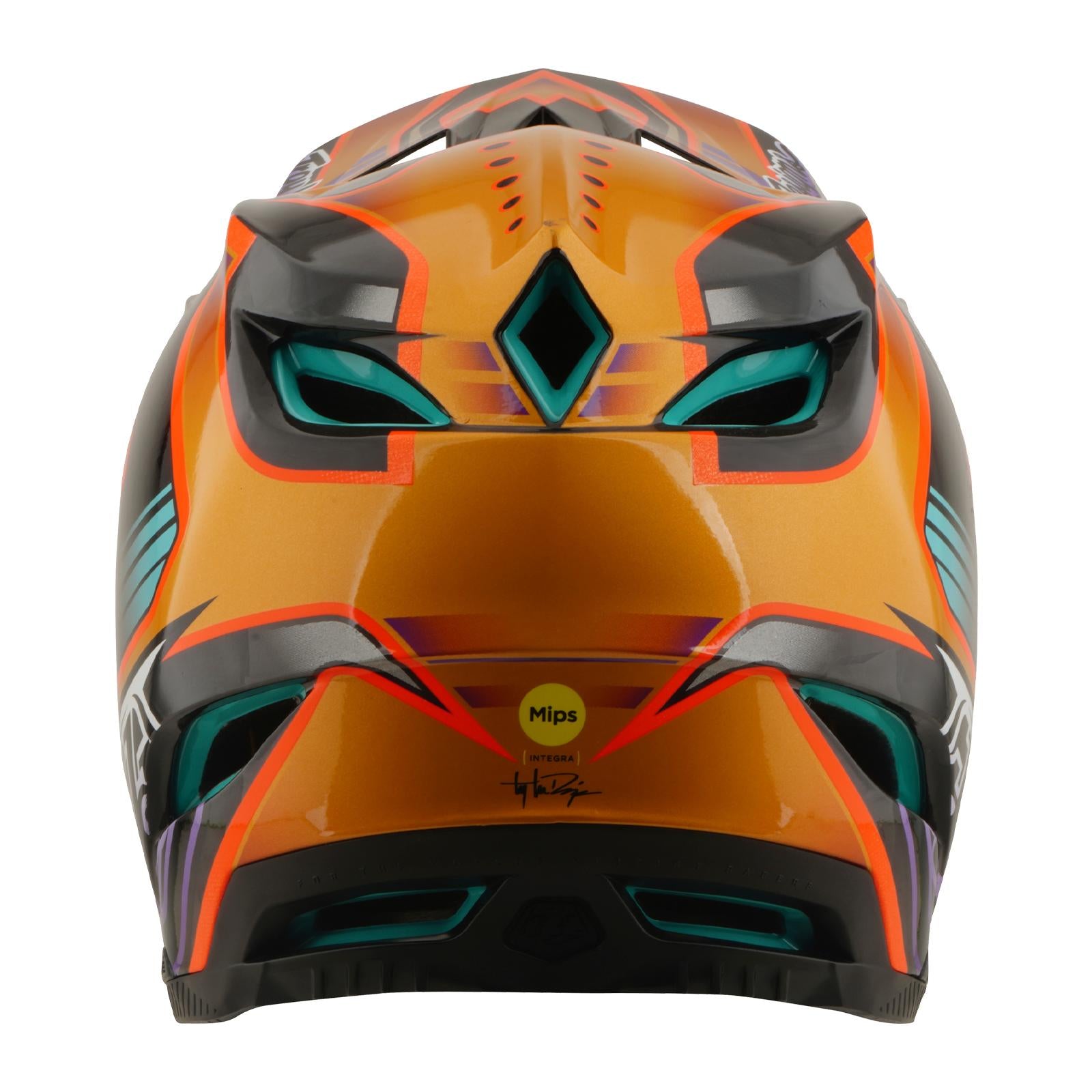 The TLD 26.1 D4 AS Carbon Helmet in Crest Gold features bold orange and black geometric designs with teal and red accents, a full-face build, and a visible "Mips" safety sticker on the back.