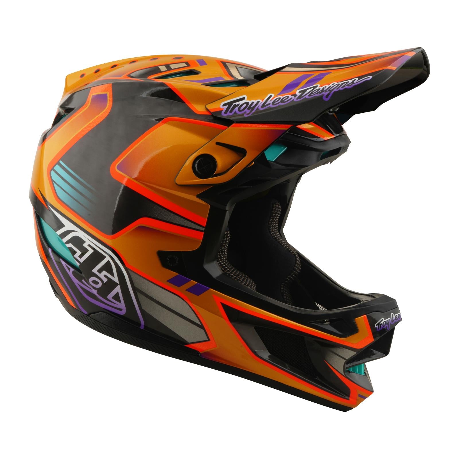 The TLD 26.1 D4 AS Carbon Helmet in Crest Gold is a full-face mountain biking helmet with an aerodynamic design, colorful accents, Mips protection, and "Troy Lee Designs" branding on the visor and chin area.