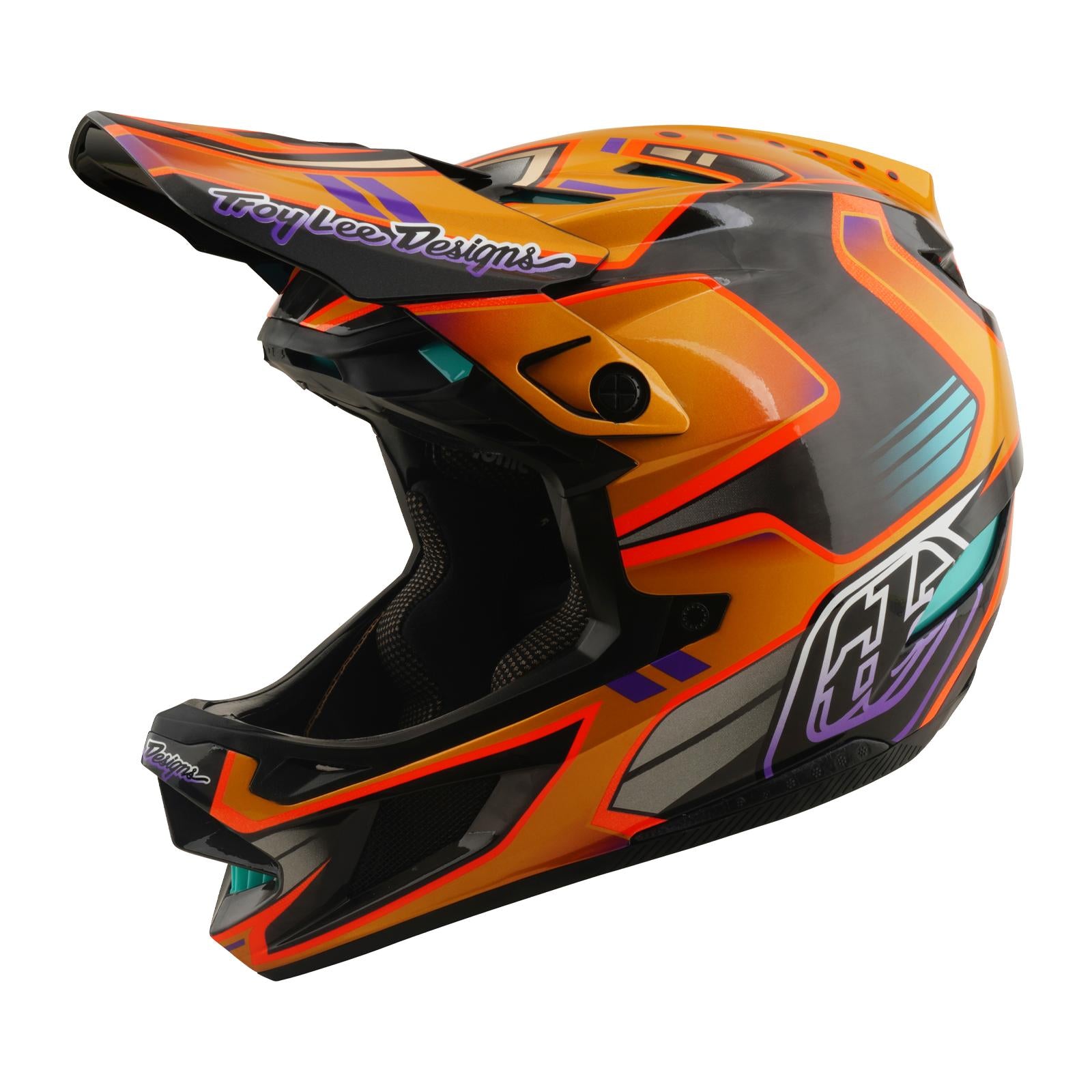 The TLD 26.1 D4 AS Carbon Helmet / Crest Gold is a full-face mountain biking helmet featuring orange and black geometric patterns, teal and purple accents, Troy Lee Designs branding, and advanced Mips safety protection.