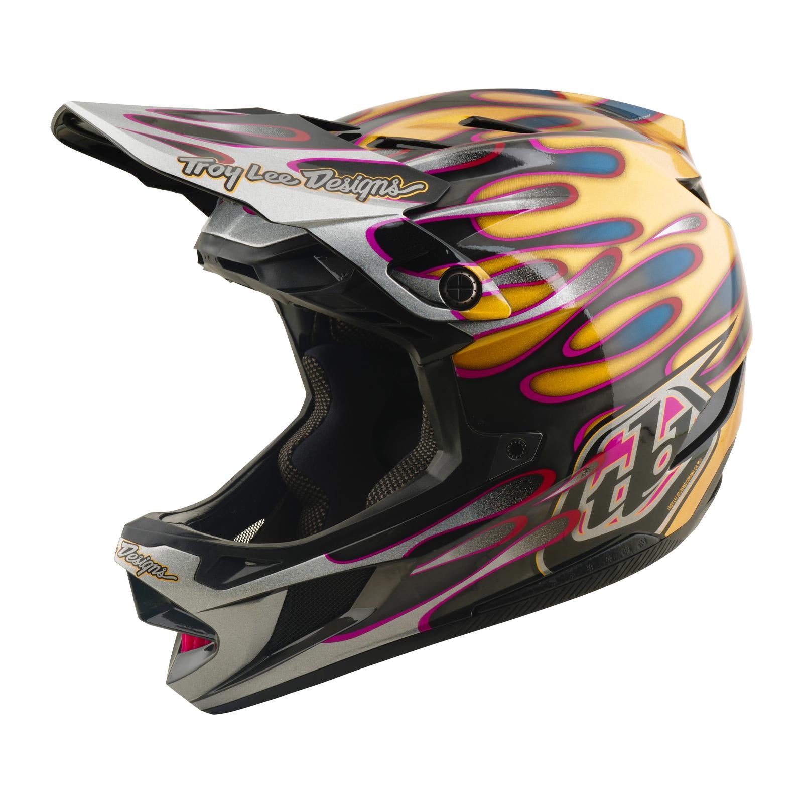 The TLD 26.1 D4 AS Carbon Helmet in Overspray Gold/Black features a striking flame design, large visor, Troy Lee Designs branding, and advanced Mips protection for enhanced downhill mountain biking safety.