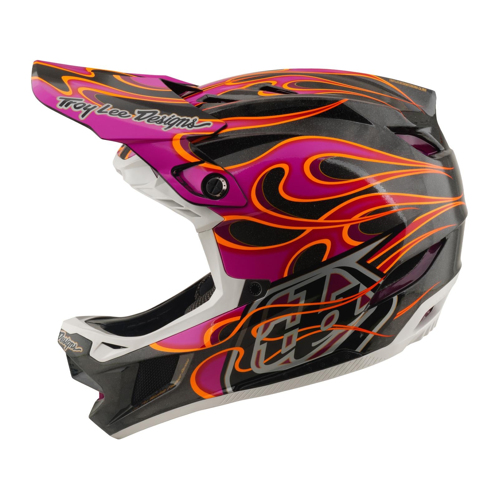 The TLD 26.1 D4 AS Carbon Helmet in Torched Carbon/Magenta features a full-face design, Mips protection, visor, and "Troy Lee Designs" branding with black, pink, and orange flame graphics.
