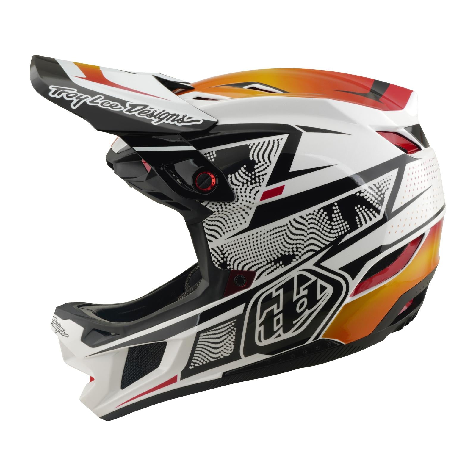 The TLD 26.1 D4 AS Composite Helmet / Lined Up White is a full-face motocross helmet with a white, black, orange, and red graphic design, Mips protection for safety, and the "Troy Lee Designs" logo on the visor.