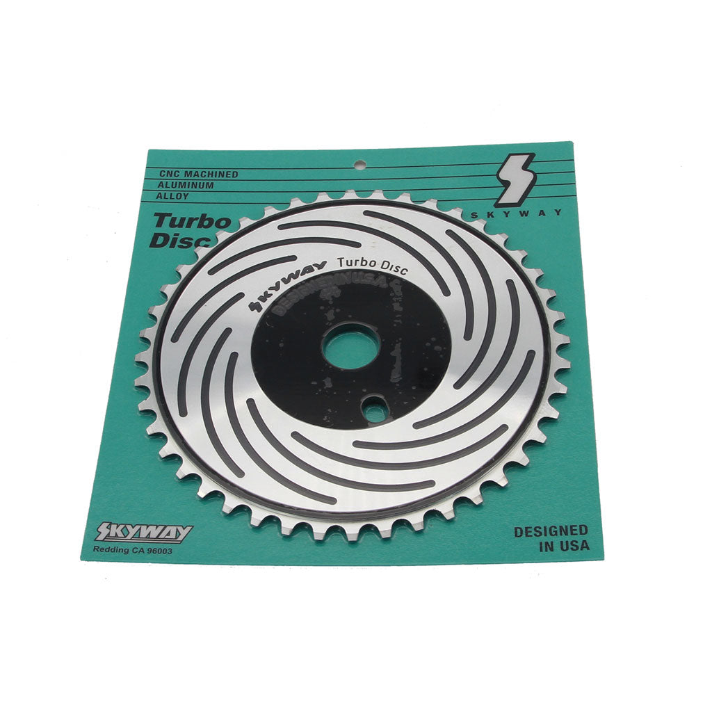 A Skyway Turbo Disc Front Sprocket in silver and black, attached to a green and black package, labeled "Skyway Turbo Disc." The package indicates it is CNC machined from 6061 Aluminum alloy, designed in the USA.