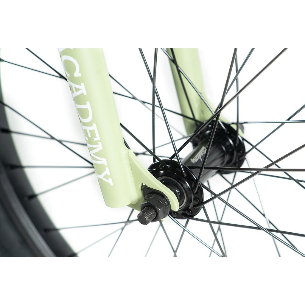 Close-up of the Academy Aspire 20 Inch Bike's front wheel, showing black spokes, axle, and a light green fork with "ACADEMY" branding—an excellent entry-level freestyle BMX featuring sealed hubs for smooth rides.