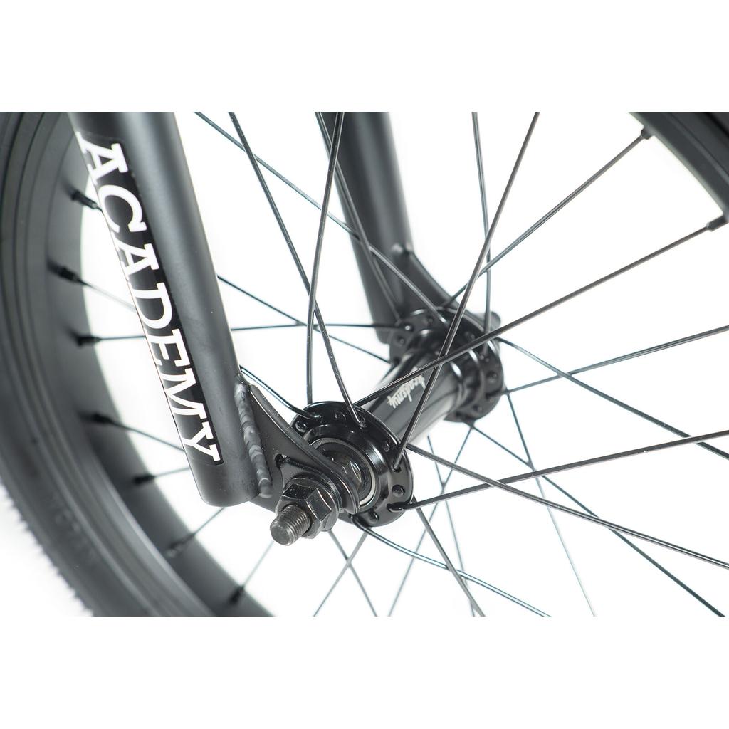 Close-up of the Academy Inspire 16 Inch Bike’s front wheel, showcasing sealed hubs, intricate spokes, detailed axle, and a fork labeled "ACADEMY" in white text.