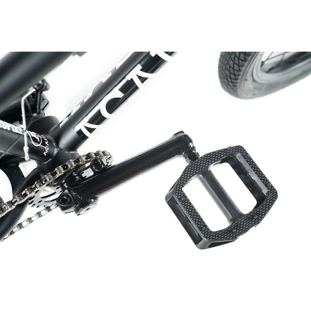 Close-up of a black pedal, crank arm, and chainring with part of the rear wheel and double wall rims—perfect for the Academy Inspire 16 Inch Bike BMX.