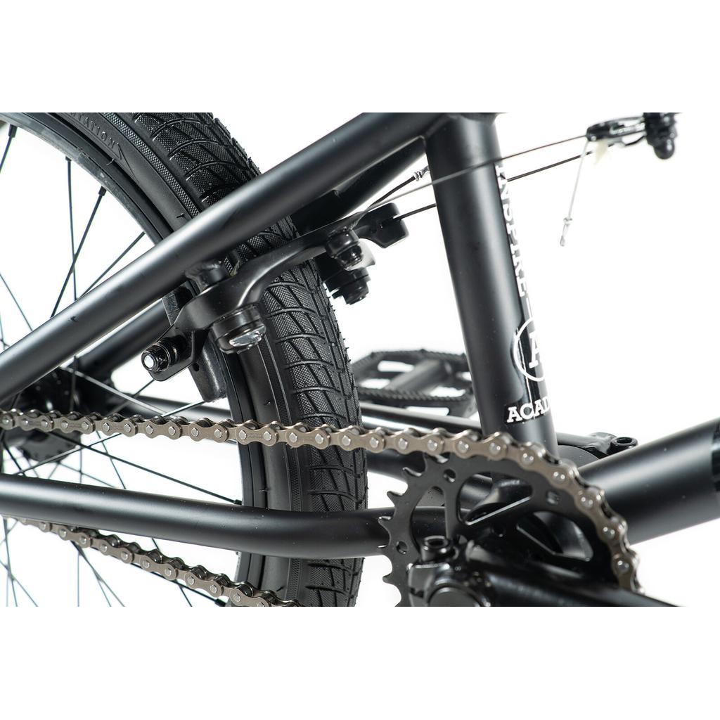 Close-up view of the Academy Inspire 18 Bike’s rear frame, highlighting the chain, sprocket, tire, brake, and part of the pedal.