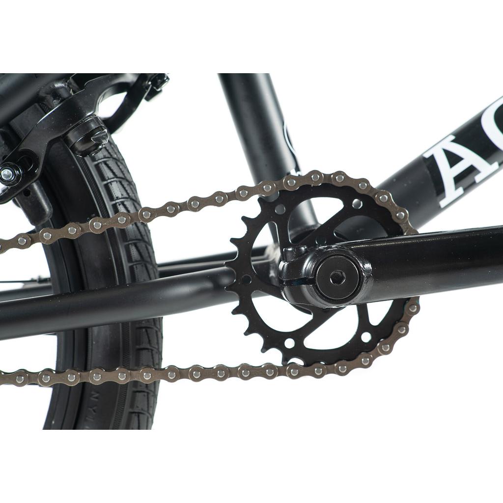 Close-up view of the Academy Inspire 18 Bike drivetrain, highlighting the chain, chainring, crank arm, and rear tire against a white background.