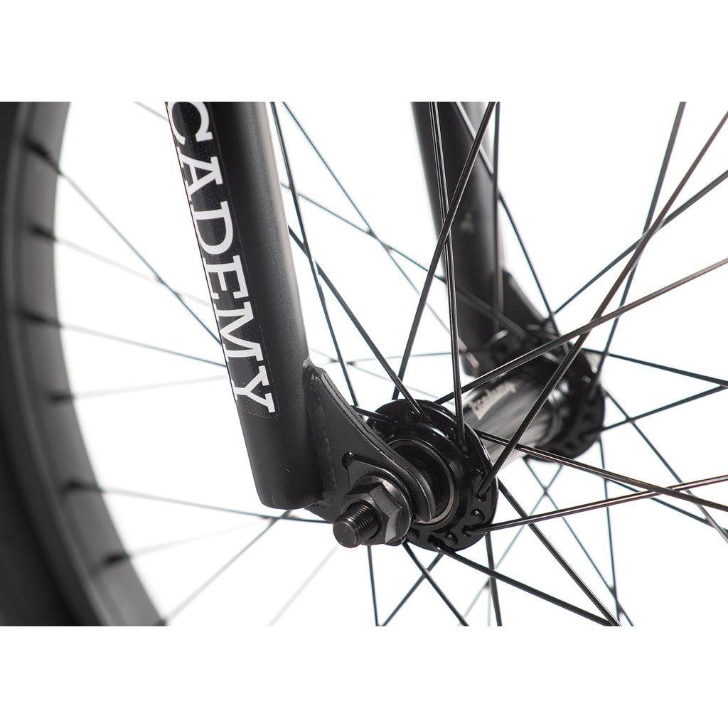Close-up of a bicycle wheel with black spokes, highlighting the fork adorned with "ACADEMY" in white letters, showcasing the sleek design and durable Hi-Ten steel frame of the Academy Trooper 20 Inch Bike.