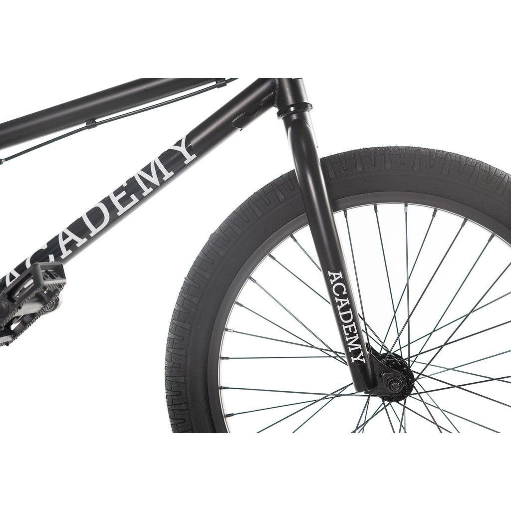 Close-up of the Academy Trooper 20 Inch Bike's black front wheel and Hi-Ten steel frame, featuring the word "Academy" printed on both the frame and fork.
