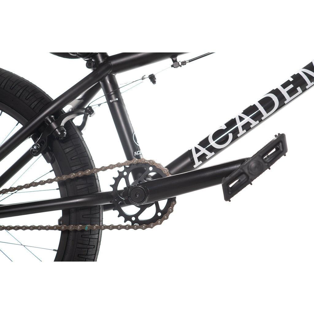 Close-up of the BMX bike drivetrain on the Academy Trooper 20 Inch Bike, highlighting the pedal, chain, and a section of the Hi-Ten steel frame with "ACAD" prominently displayed in white letters.