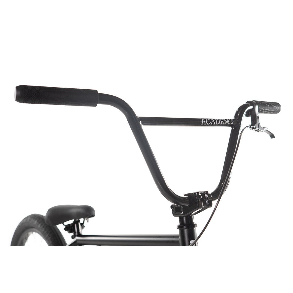 Close-up of the handlebars of the Academy Trooper 20 Inch Bike, prominently displaying the "ACADEMY" logo. The shot highlights the grips and brake lever, emphasizing the sturdy design and quality craftsmanship of its Hi-Ten steel frame against a pristine white background.