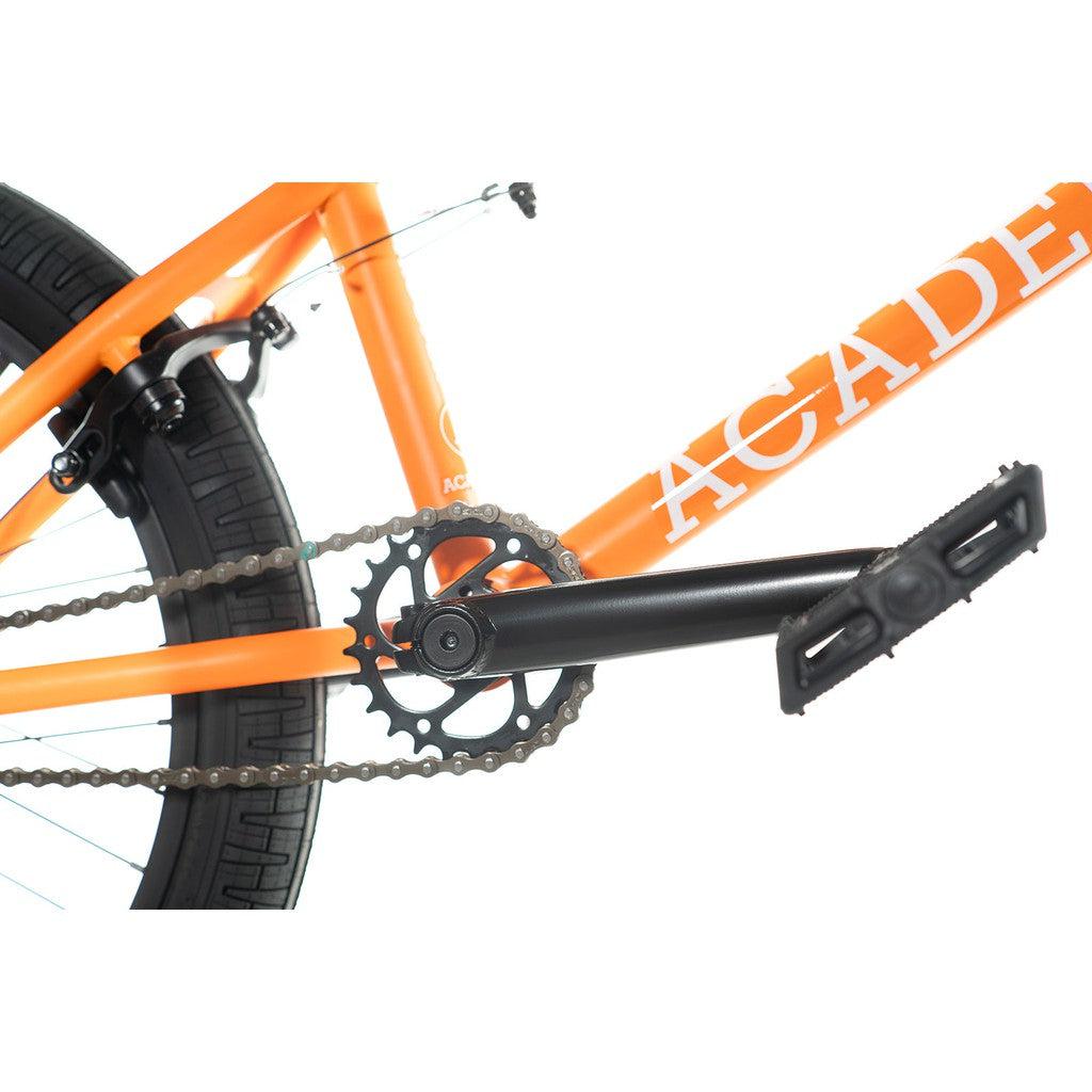 Close-up of the Academy Trooper 20 Inch Bike's orange BMX frame highlighting the rear wheel with sealed hubs, black pedal, chain, and sprocket gears.