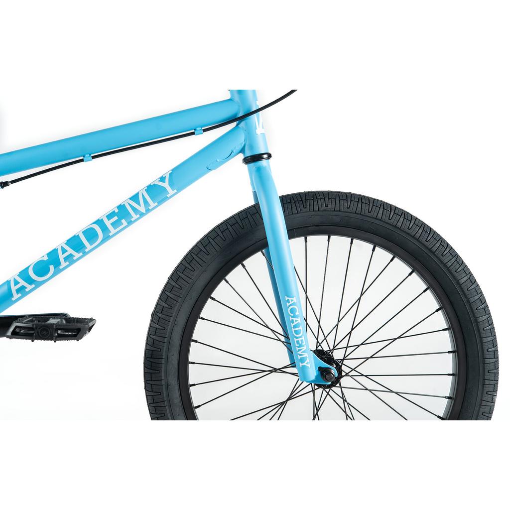 Close-up of the front half of the Academy Trooper 20 Inch Bike, an entry-level BMX in light blue with black tire, spokes, and pedal. "ACADEMY" is printed in white on both the frame and fork.